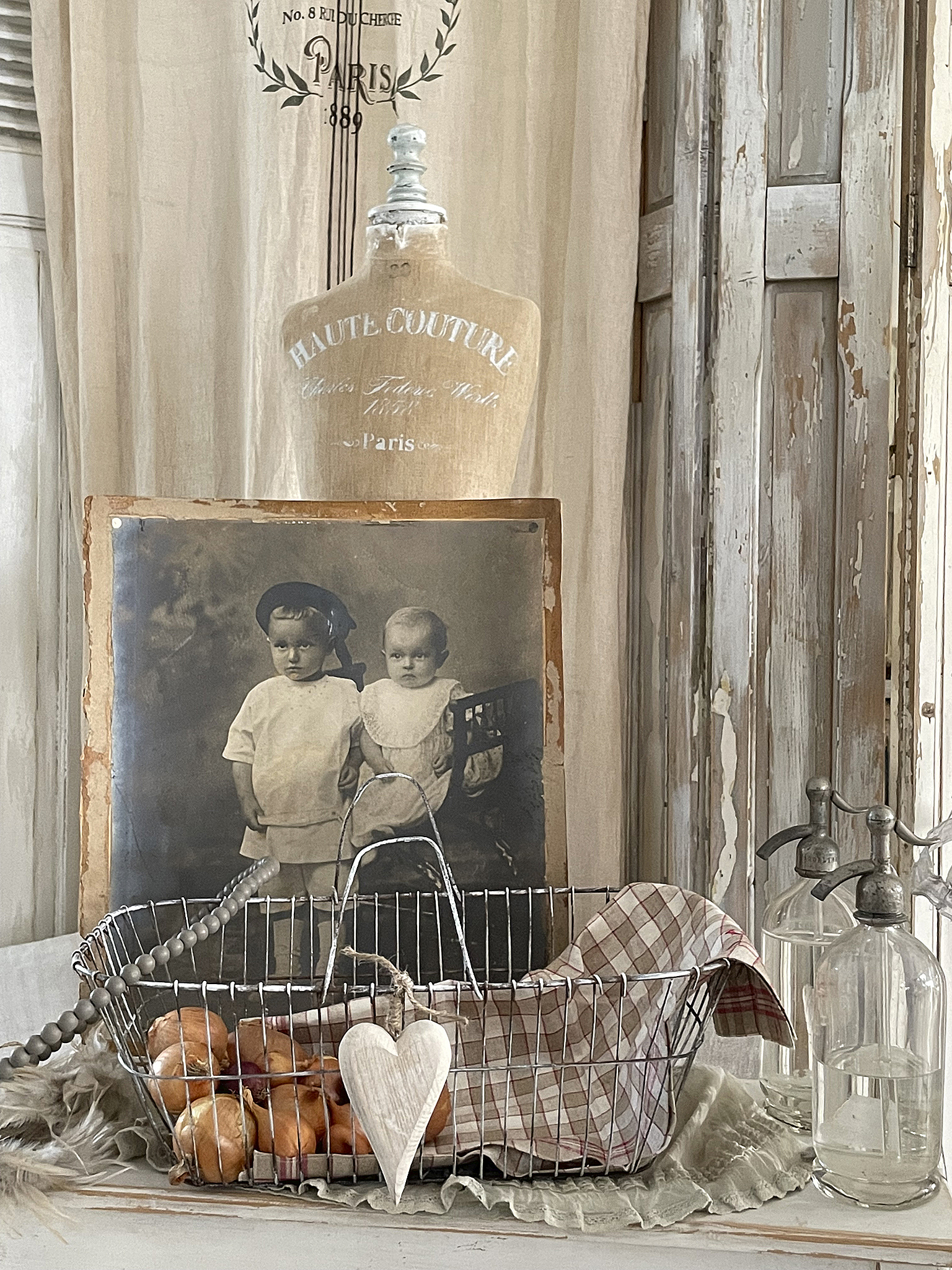 Vintage Dekoration mit nostalgischem Foto und Drahtkorb Nostalgisches Stillleben mit einem alten Foto, einem Drahtkorb mit Zwiebeln und einem Schneiderpuppen-Display