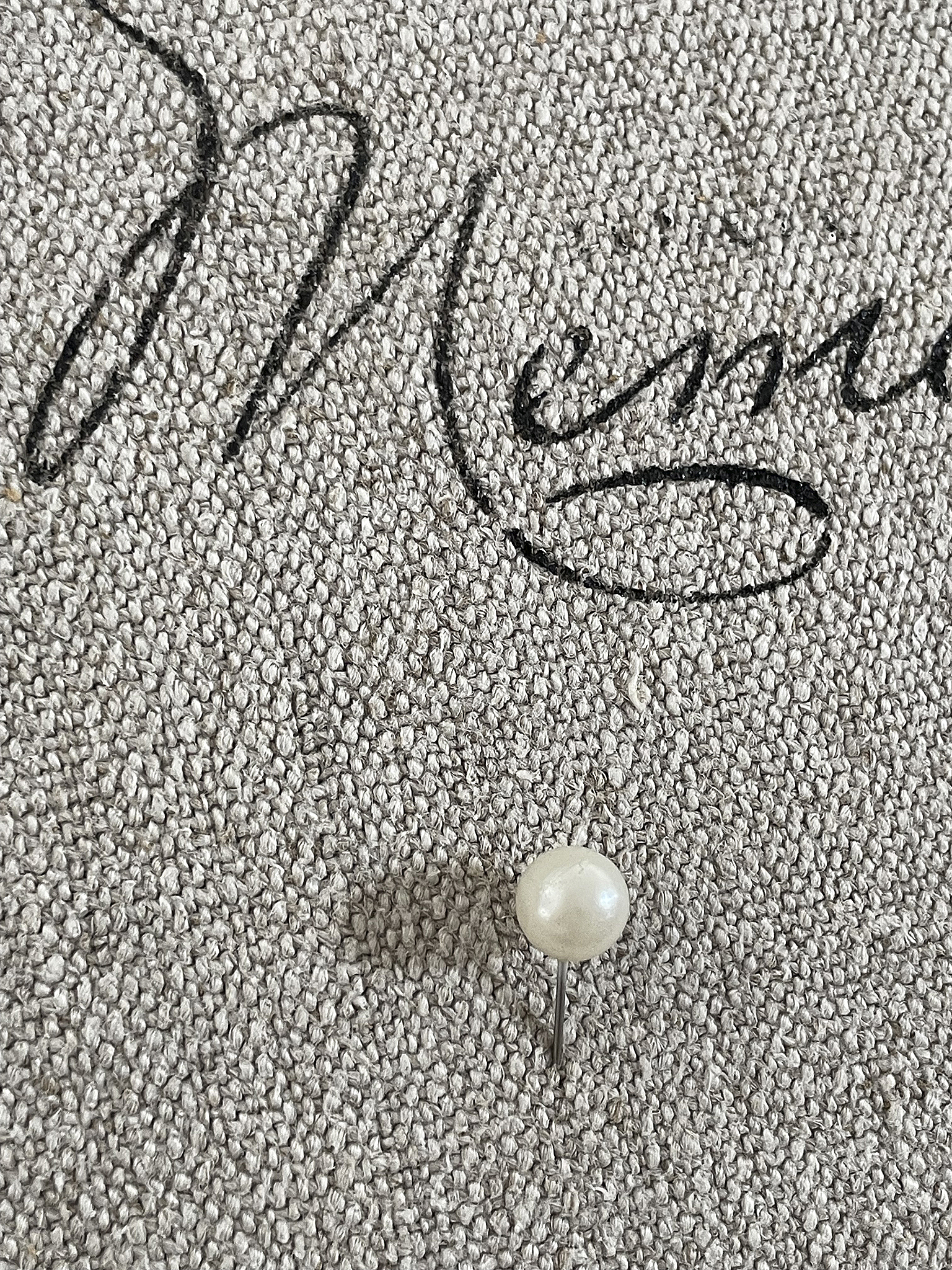 Elegante Perlenstecknadel auf grauem Untergrund Perlenstecknadel aus Metall mit weißer Perle auf strukturiertem grauem Stoff