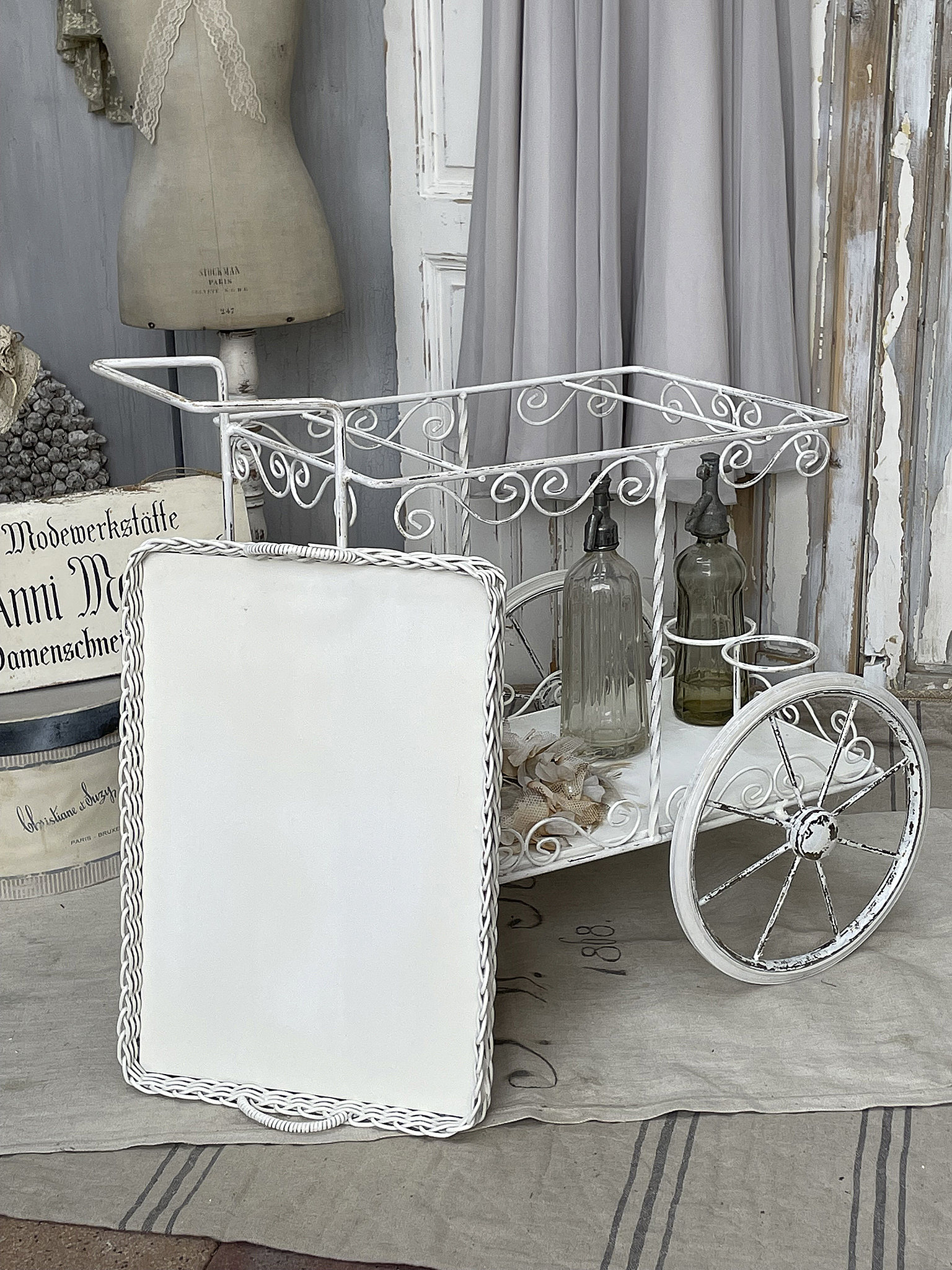 Eleganter weißer Servierwagen mit Flaschen und Dekoration Weißer Servierwagen aus Metall, bestückt mit Glasflaschen und dekorativen Elementen