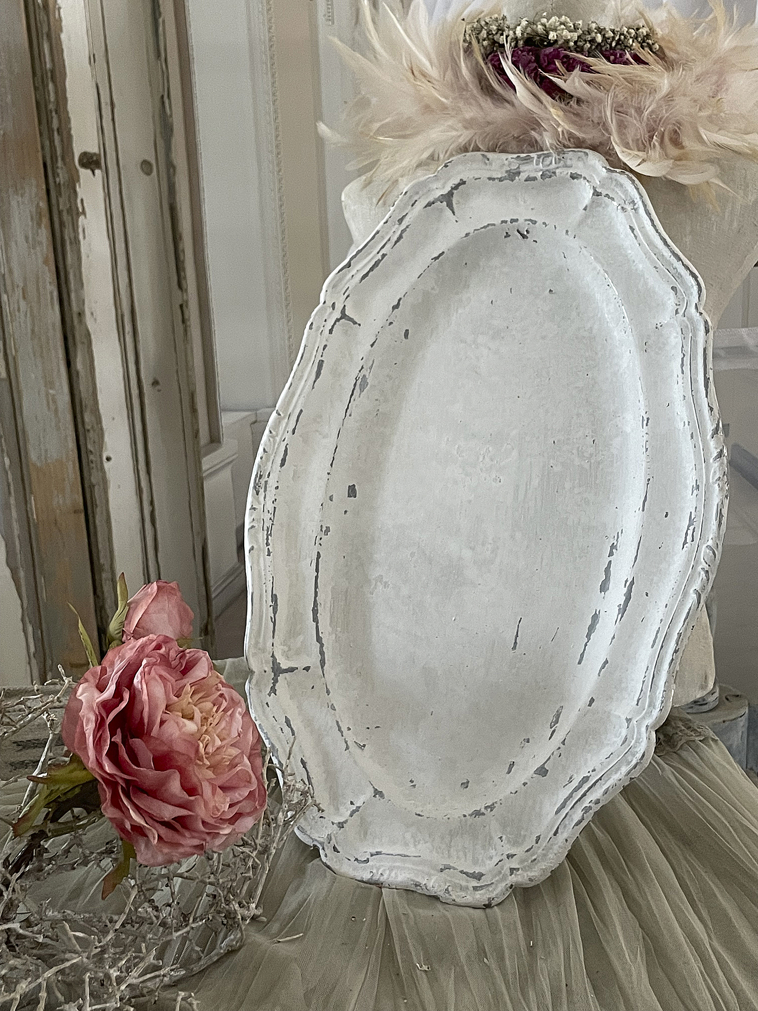 Dekorative Vintage Servierplatte mit abgeriebenem Finish, umgeben von einer rosa Rose und einer zarten Haarschmuckdekoration.
