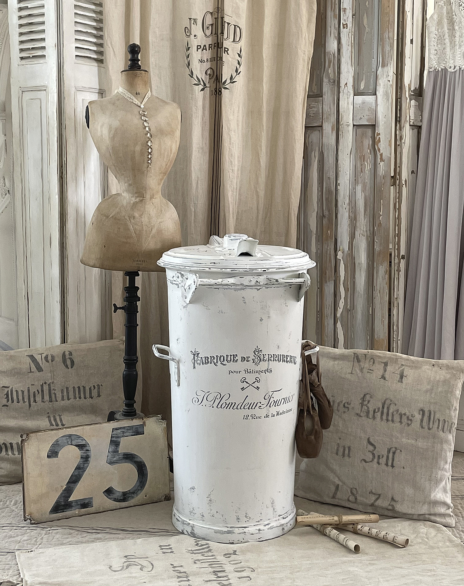 Dekorative Vintage-Dekoration mit weißem Behälter und Schneiderpuppe Ein kunstvoll gestalteter Raum mit einer weißen Deko-Tonne, einer Schneiderpuppe und stilvollen Textilien.