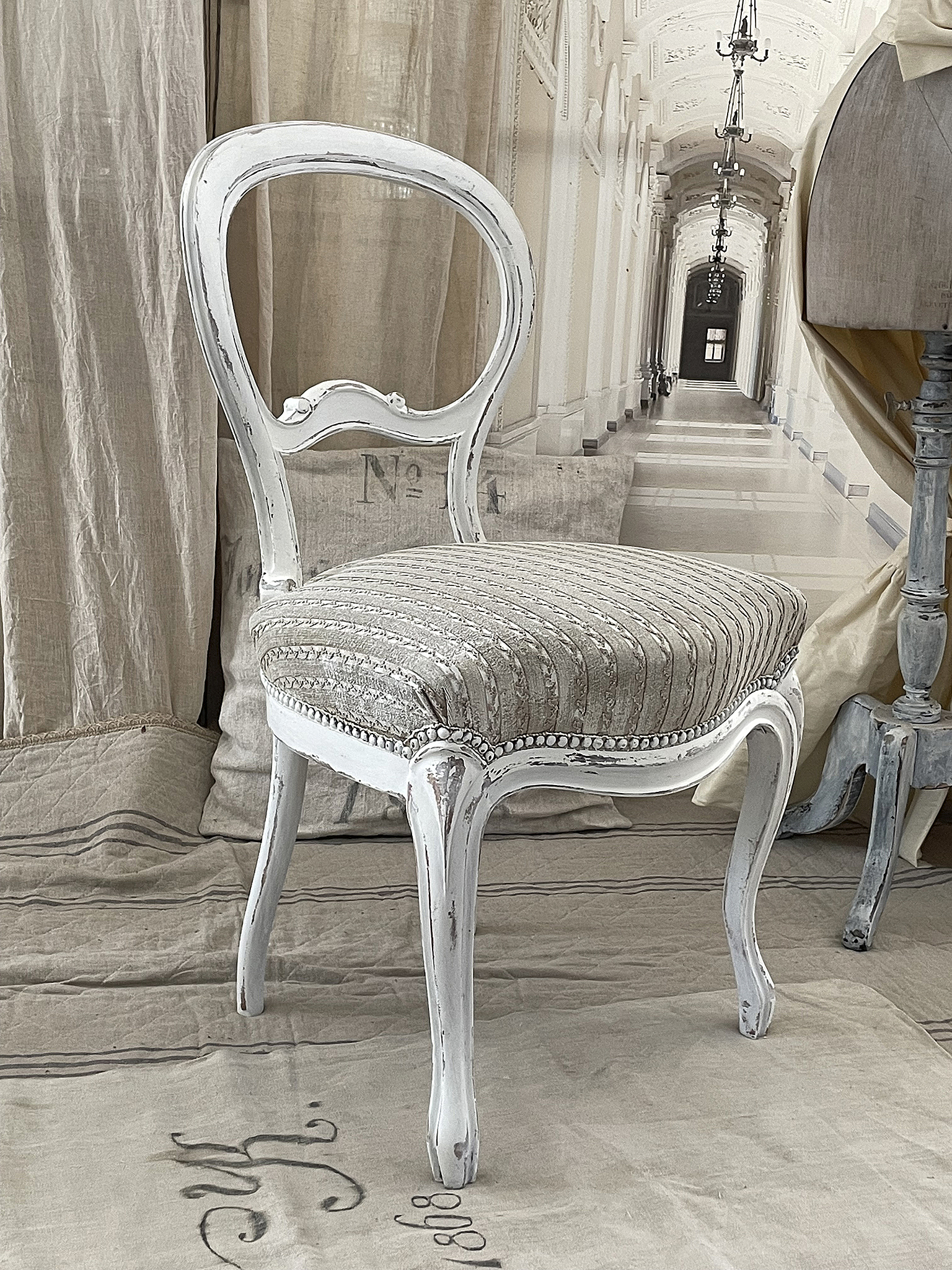 Eleganter weißer Stuhl mit gestreutem Bezug für nostalgisches Ambiente Weißer Stuhl mit gepolsterter Sitzfläche und geschwungenen Beinen in einem stilvollen Raum
