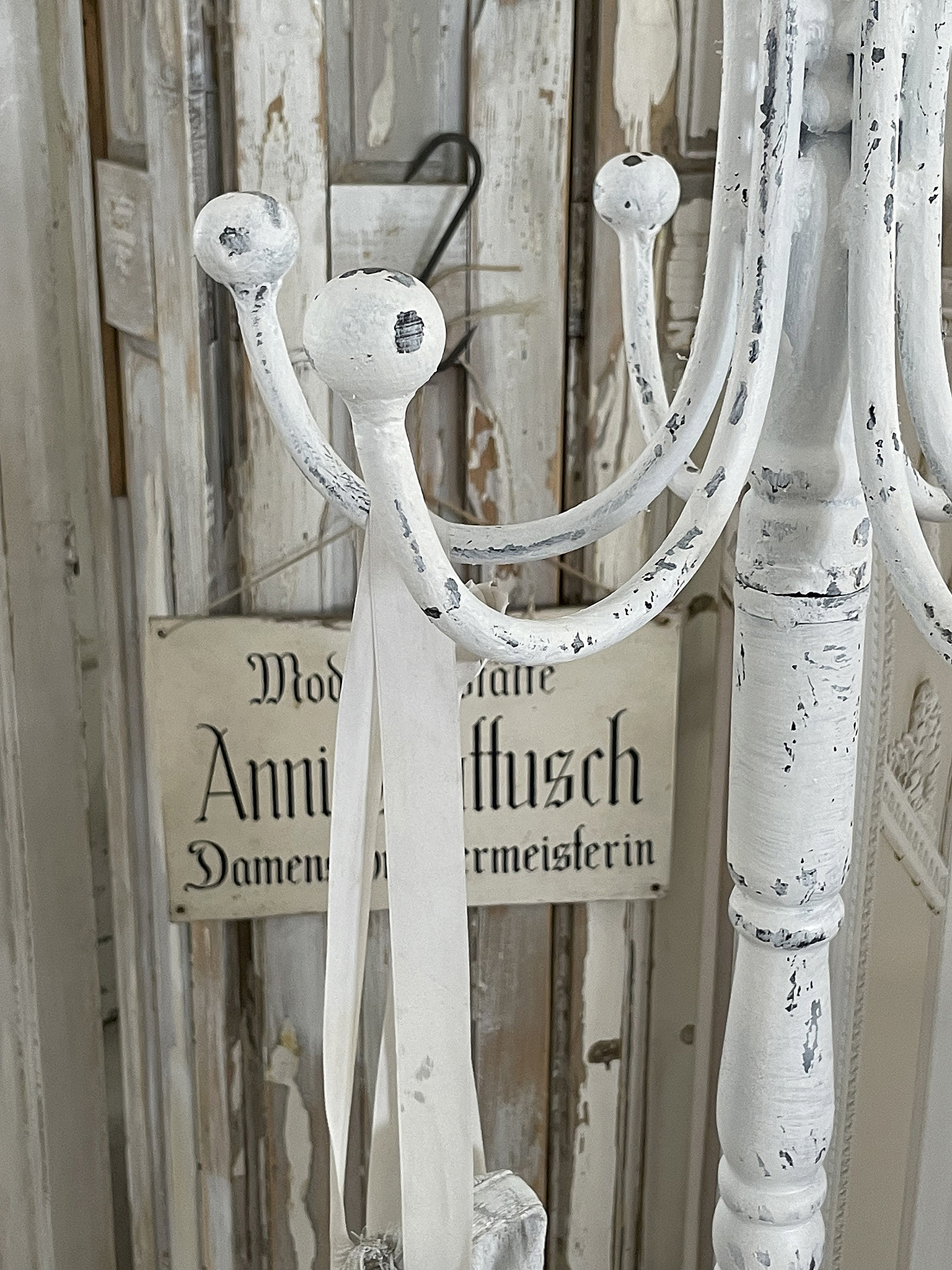 Kleiderständer im vintage Stil mit nostalgischem Schild Detailaufnahme eines weißen Kleiderständers mit gekreuzten Armen und einem nostalgischen Schild im Hintergrund.