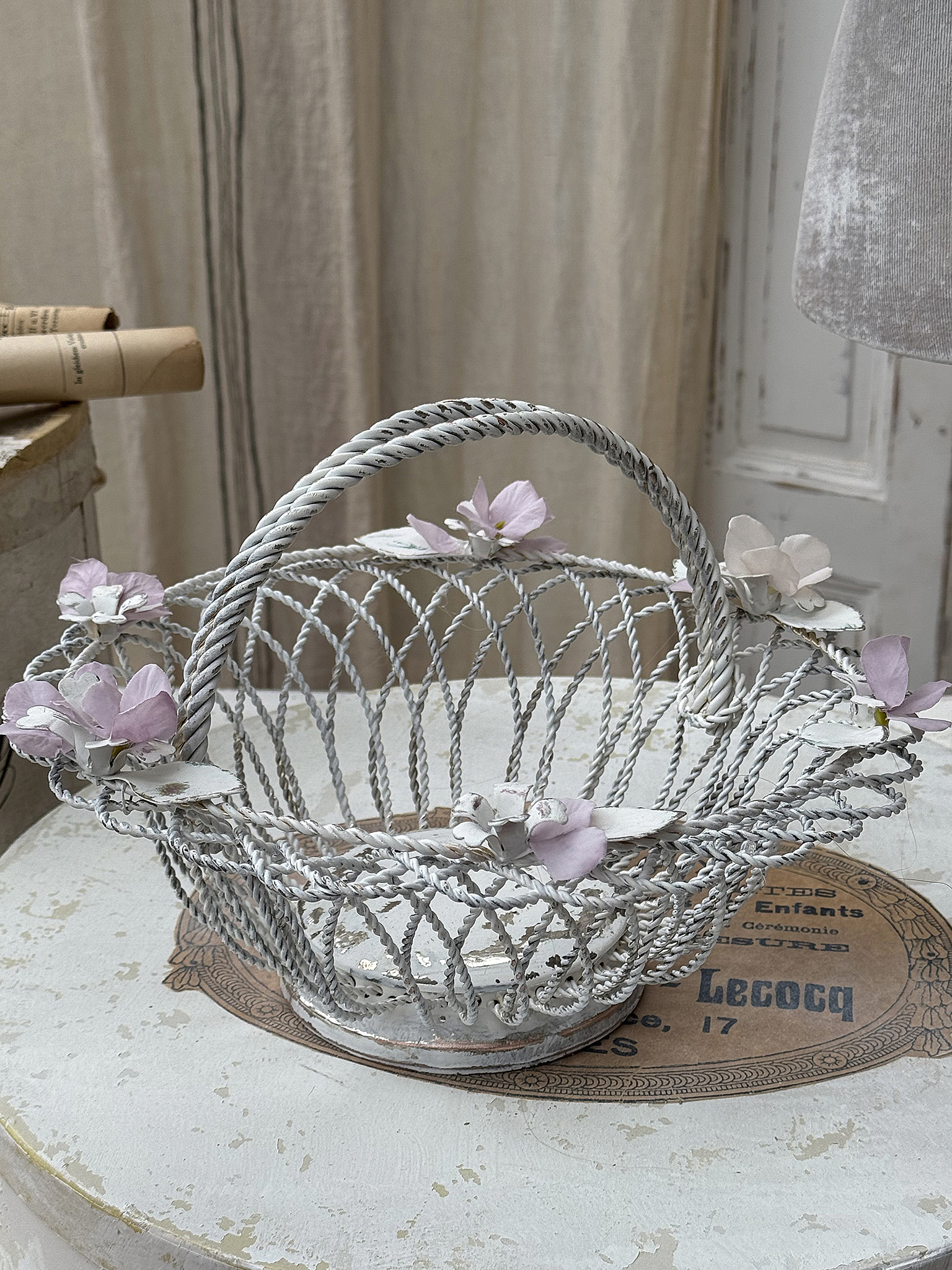 Klassischer dekorativer Korb mit Blumen Dekorativer, geflochtener Korb in Weiß mit zarten Blumen, auf einem Vintage-Tisch platziert.