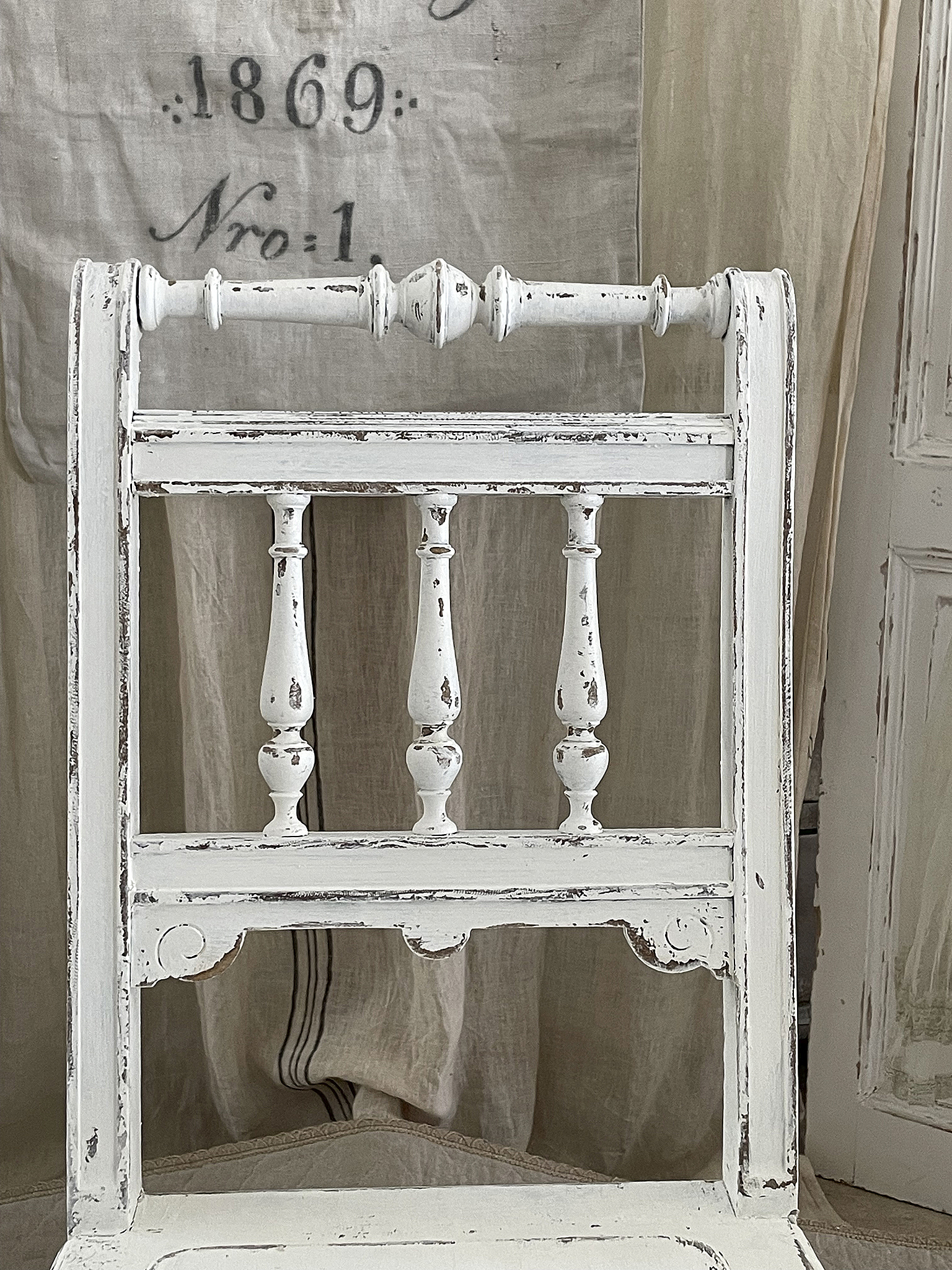 Nahaufnahme eines antiken weißen Stuhls mit verziertem Rückenteil und Vintage-Charakter