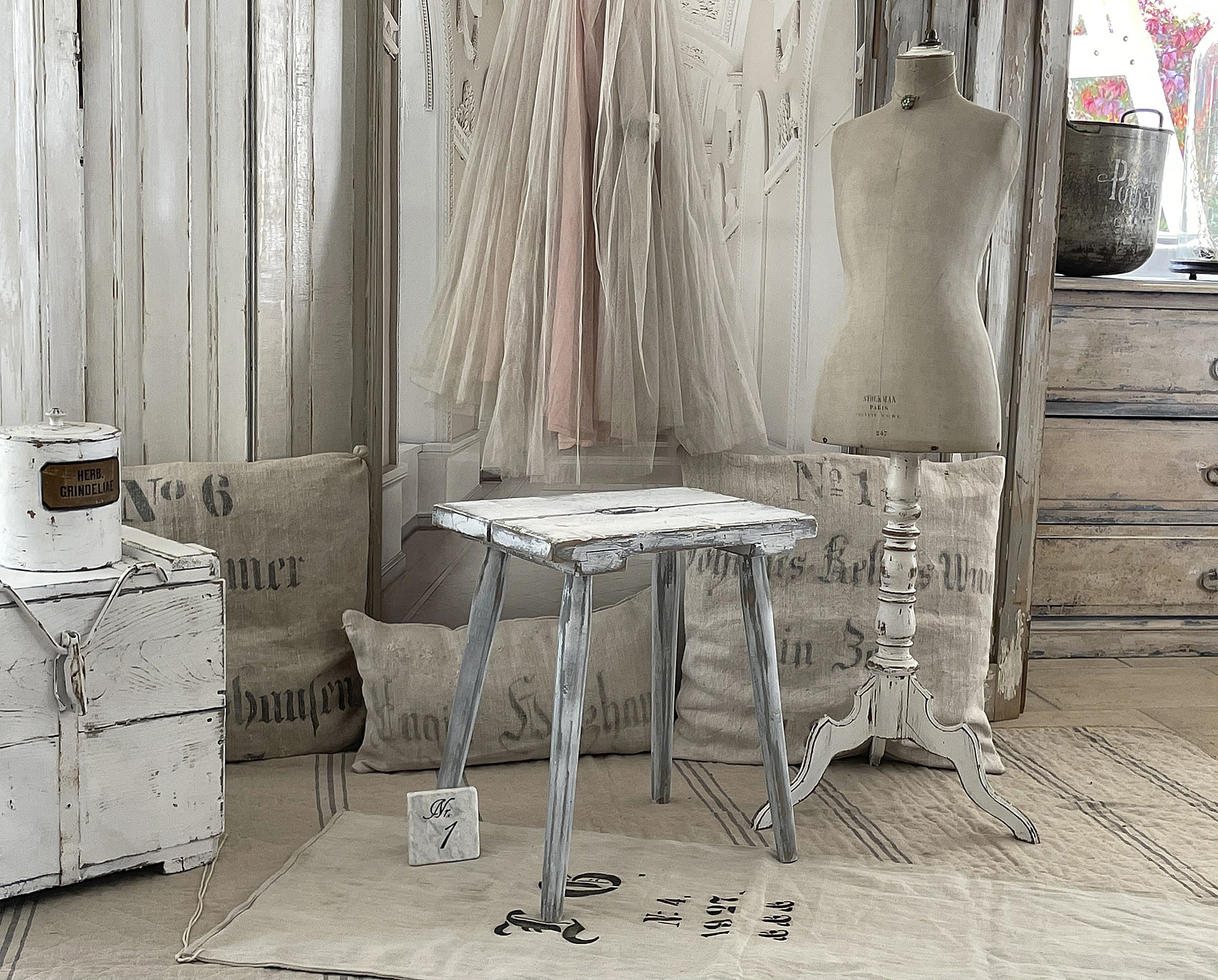 Ein dekorativer Vintage Hocker in einem eleganten Raum, umgeben von stilvollen Textilien und einem Schneiderpuppen.