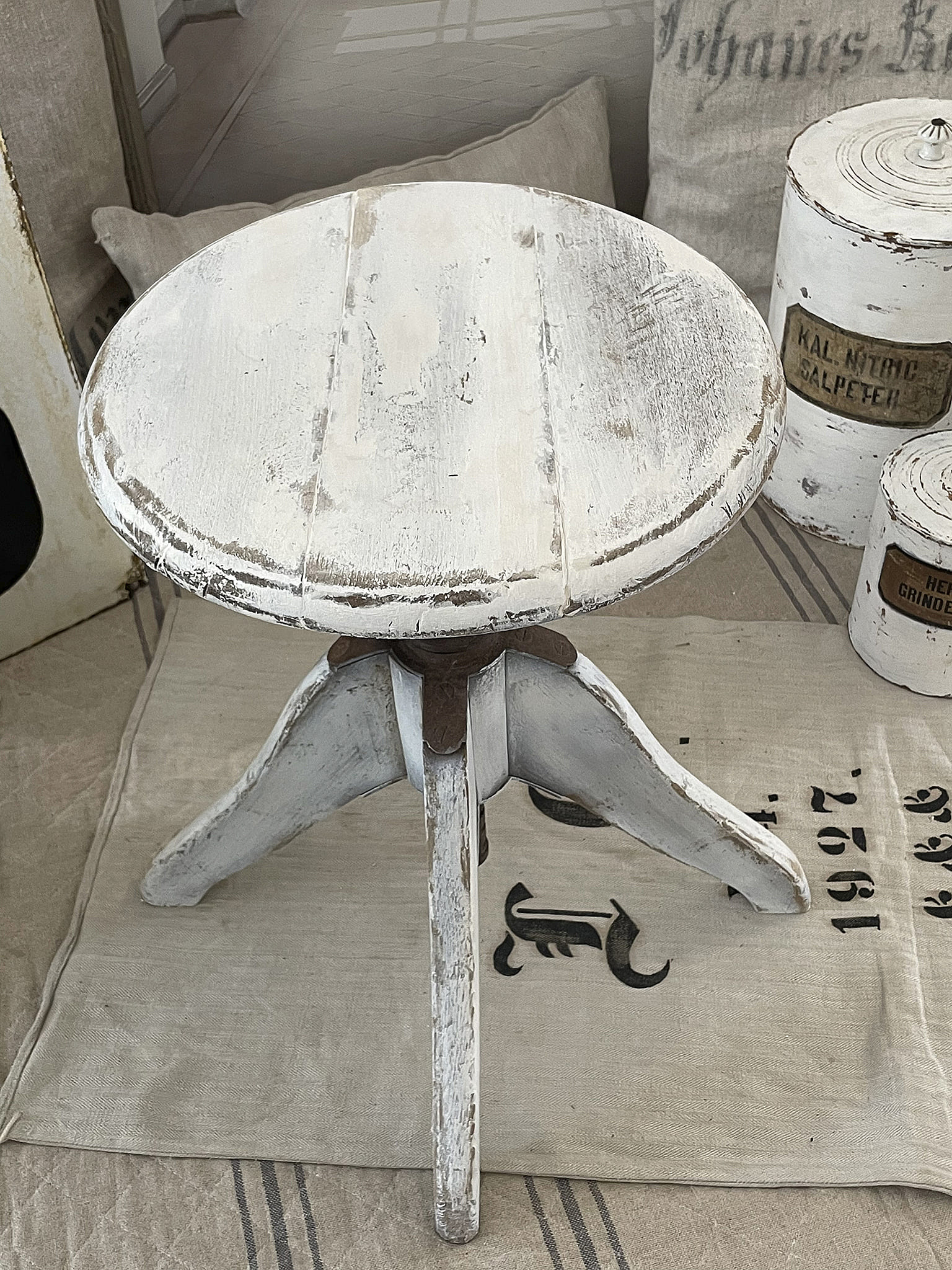 Beistelltisch aus Holz mit rundem Tischplatte und drei Beinen, weiß lackiert, auf einem Textil unterlegt.