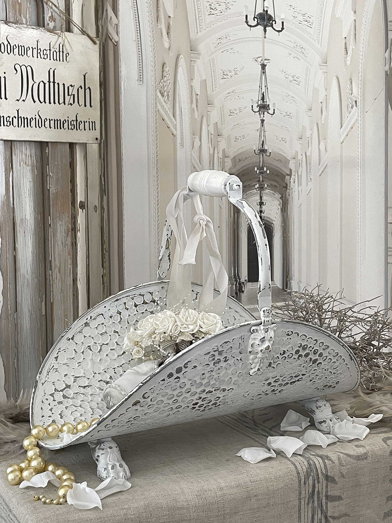 Dekorative Schale mit Blumenschmuck und Perlenkette Dekorative Schale auf weißem Tisch, geschmückt mit Blumen und Perlen, im Hintergrund ein eleganter Gang