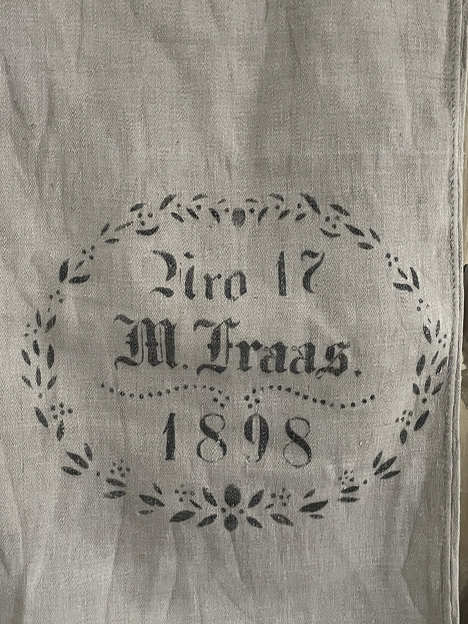 Alter Leinenstoff mit dem Druck "Biro 17 M. Fraas 1898" umgeben von einer floral gestalteten Umrandung
