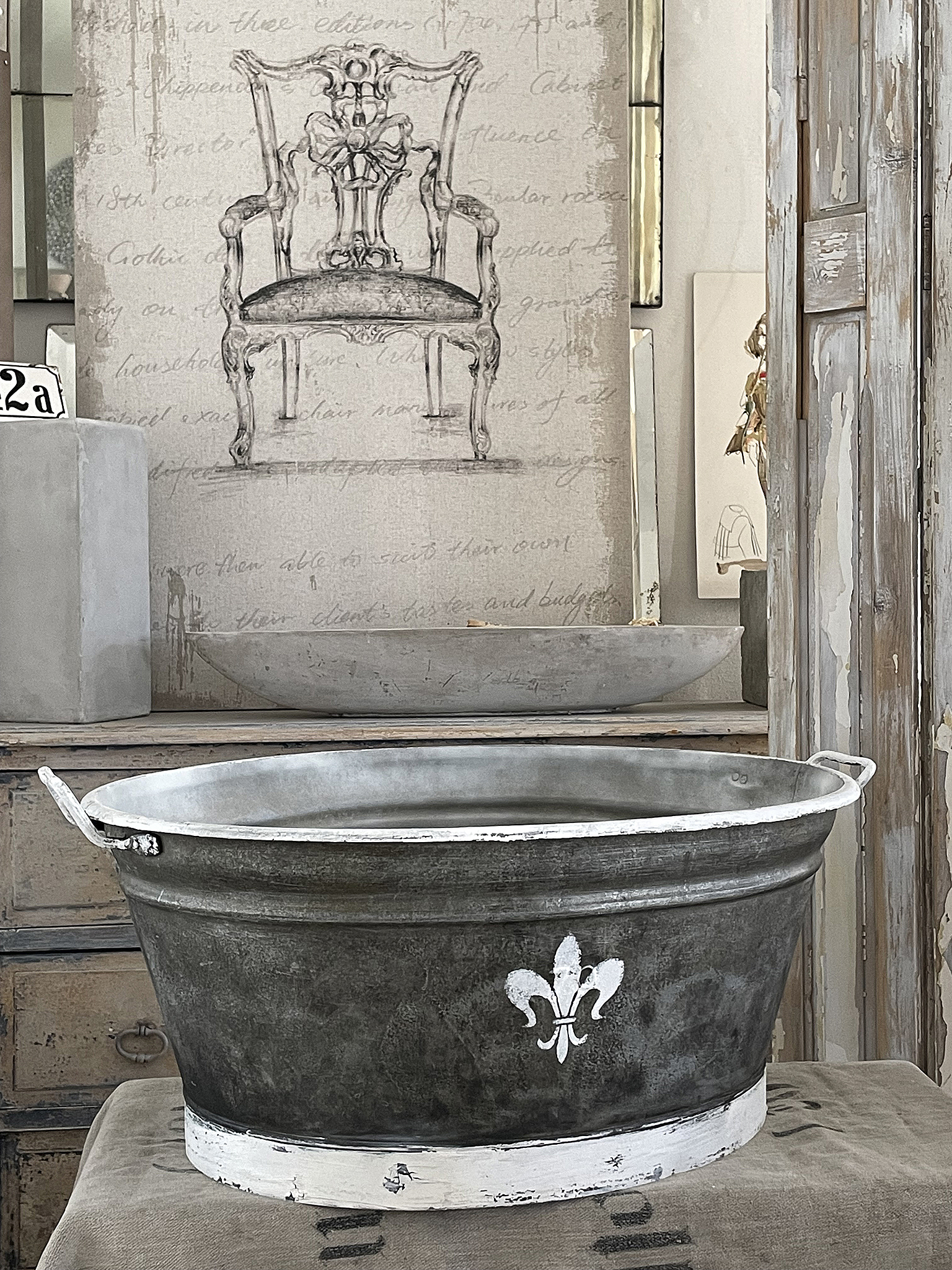 Vintage Metalleimer mit floralen Verzierungen auf Holzuntergrund Antiker Metalleimer mit einer französischen Lilie in weiß auf grünem Metall, im Hintergrund eine stilvolle Wandgestaltung mit einem Stuhl