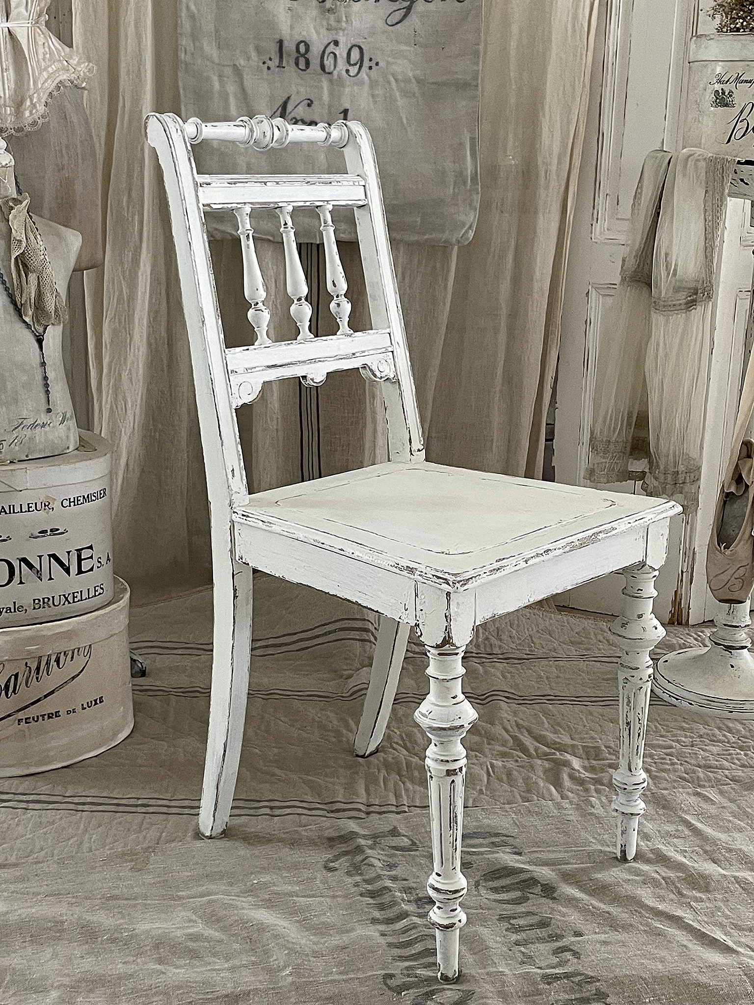 Ein eleganter, antiker Stuhl in Weiß mit kunstvoller Rückenlehne und gedrechselten Beinen.