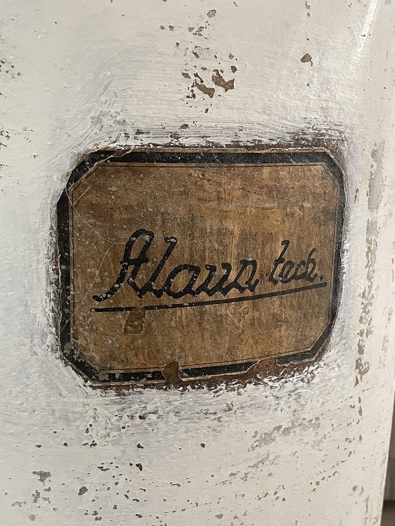 Detailaufnahme eines abgenutzten Aufklebers mit der Aufschrift "Alarms lock" auf einer weißen Oberfläche.