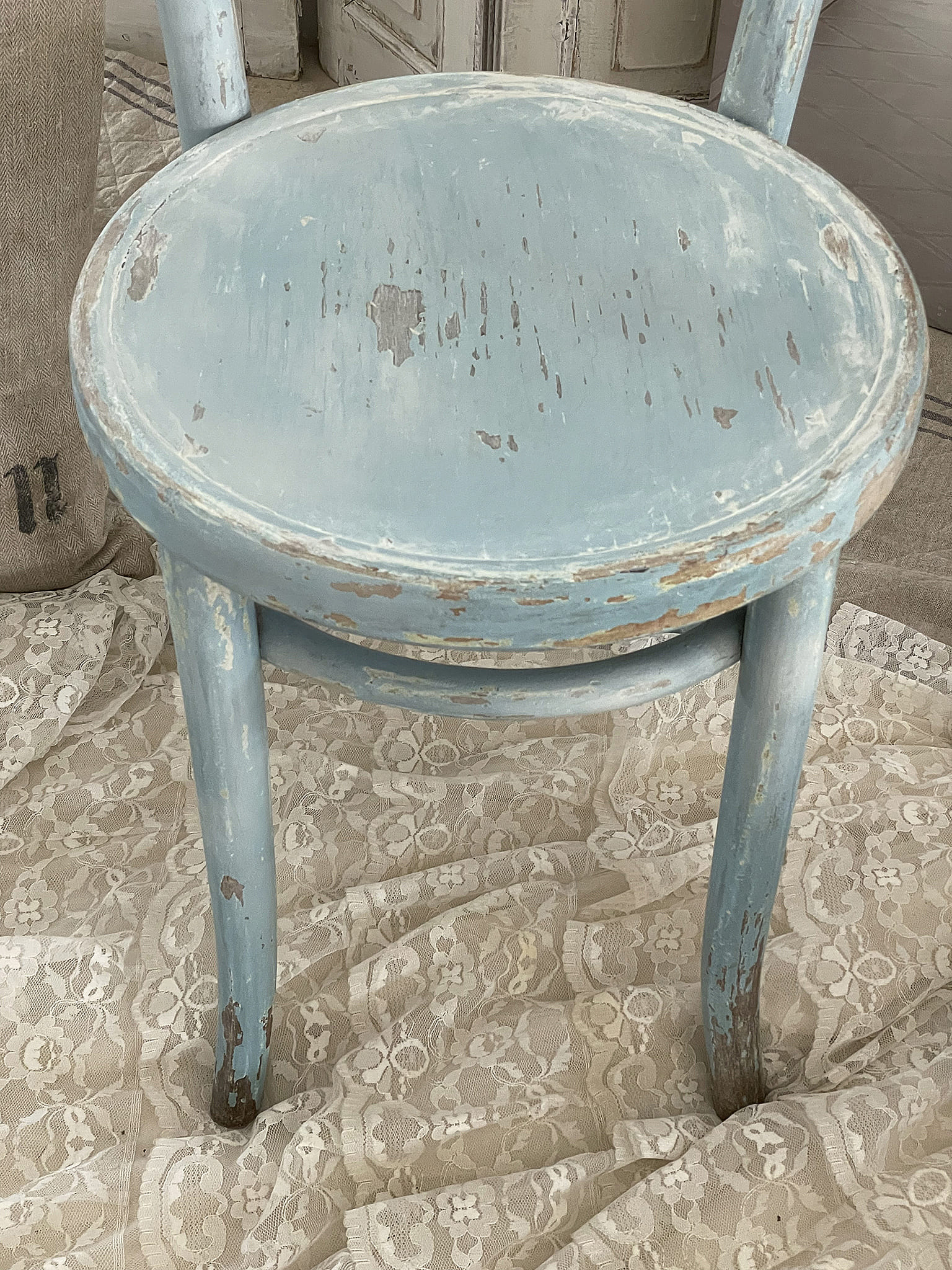 Nahaufnahme eines gebrauchten blauen Holzstuhls auf einem eleganten Spitzen-Tuch
