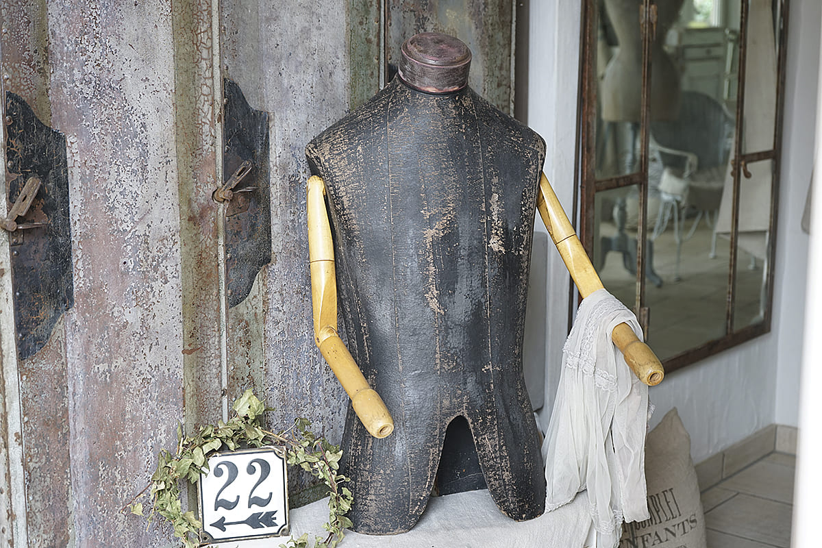 Elegante Schneiderpuppe aus schwarzem Material mit Holzarmen und einem weißen Tuch, dekoriert mit einer kleinen Zahl und einem Kranz.