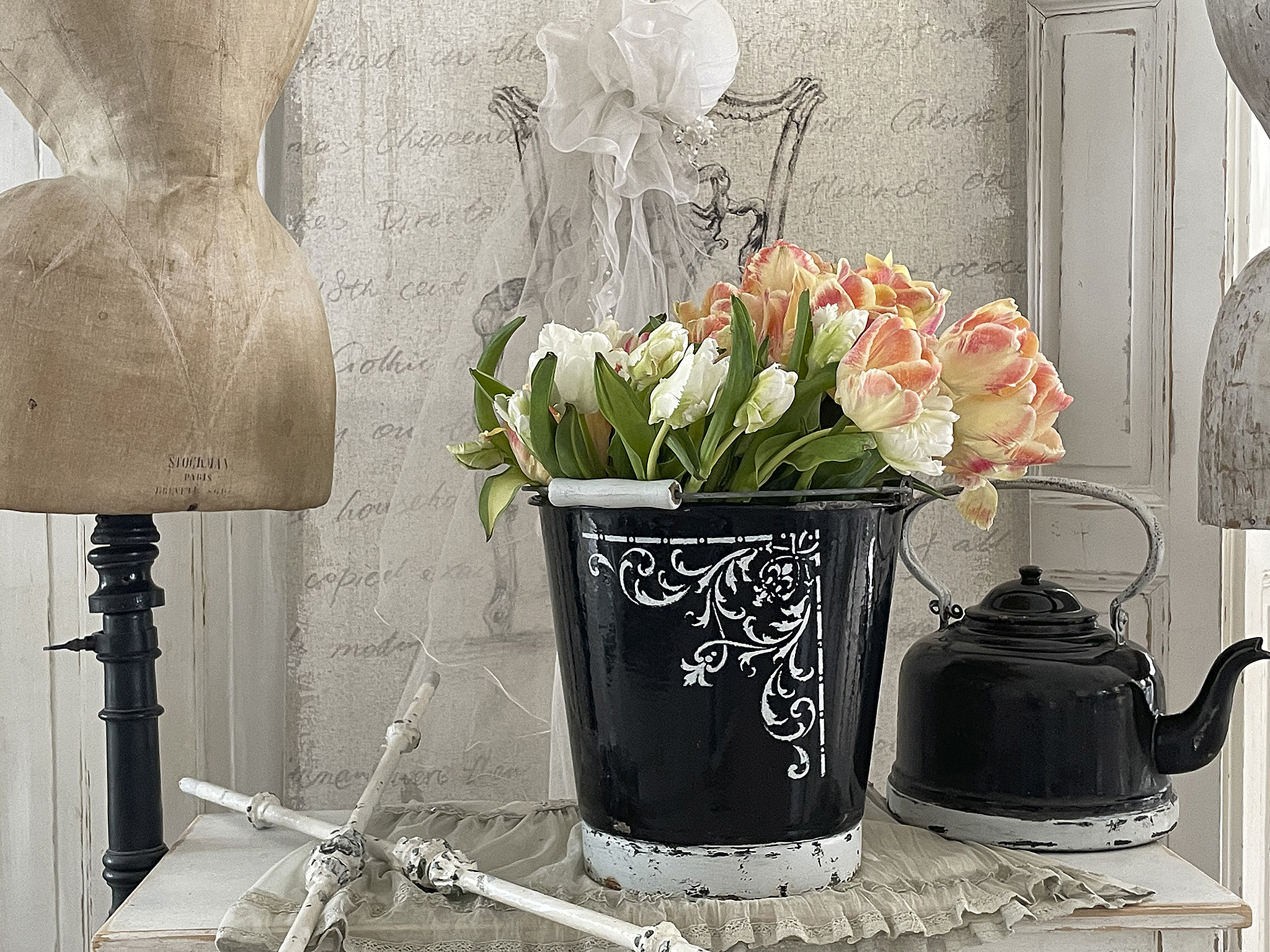 Dekorative Anordnung mit Tulpen in einer schwarzen Metallvase und einer Gießkanne auf einem Tisch