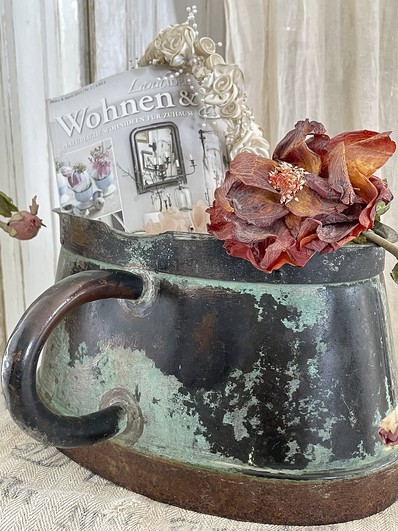 Dekorativer Antiktopf mit Zeitschrift und Blume Antiker Topf aus Metall mit einer Zeitschrift und einer getrockneten Blume auf einem Tuch