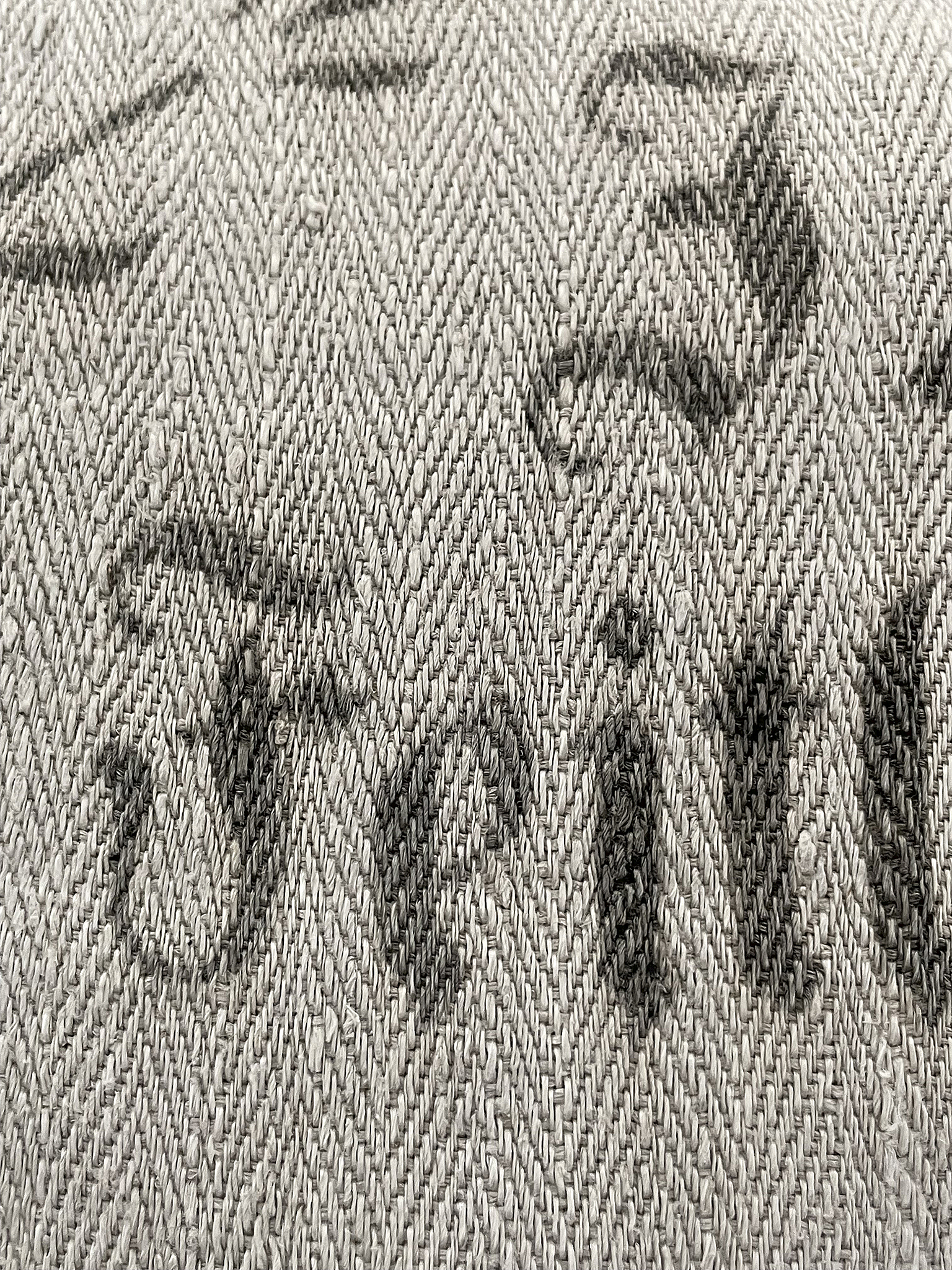 Detailaufnahme eines grauen Gewebes mit Schriftzug Nahaufnahme eines Stoffes in Grautönen mit unleserlichem Schriftzug