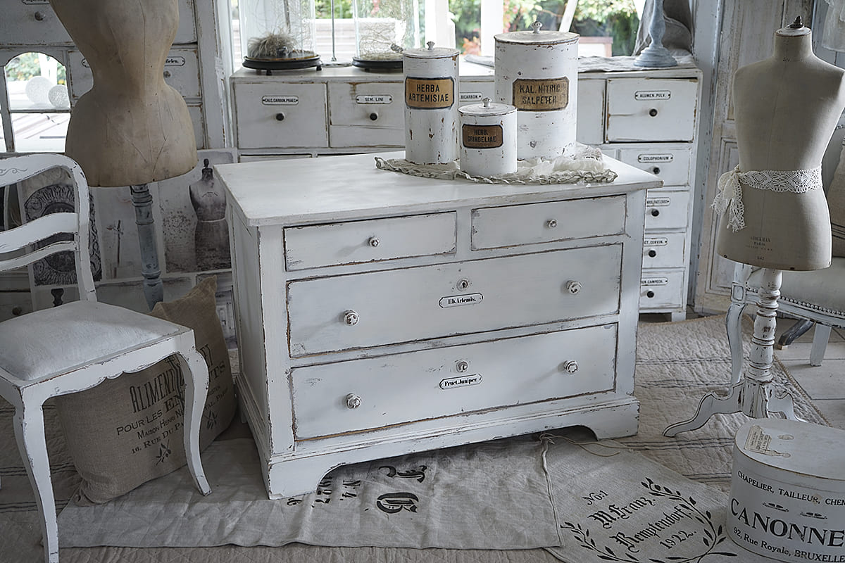 Vintage Kommode im Shabby-Chic-Stil mit Aufbewahrungsbehältern Helle Shabby-Chic-Kommode mit mehreren Schubladen und weißen Aufbewahrungsgläsern in einem stilvollen Raum.
