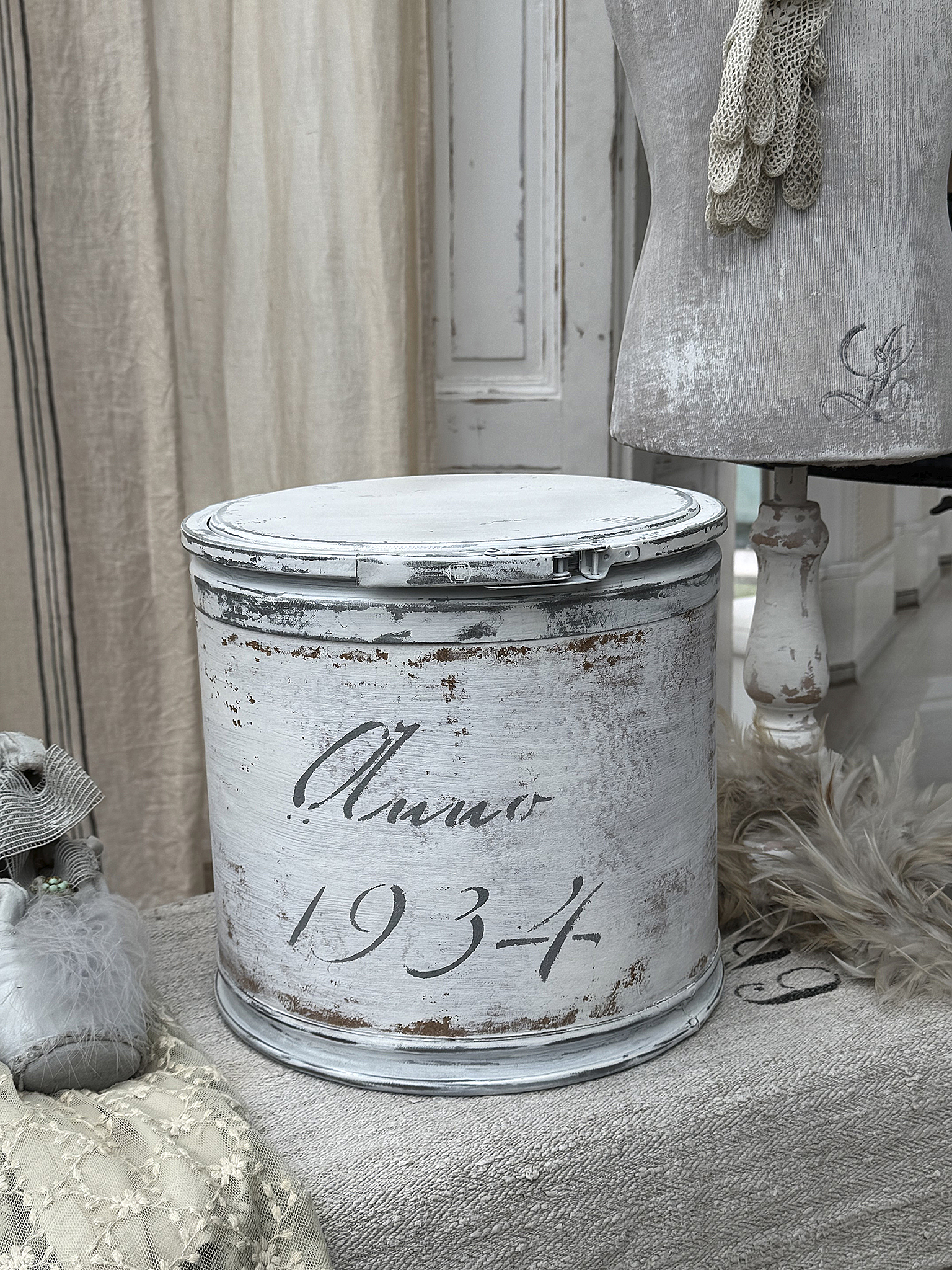 Dekorativer Vintage-Bereich mit weißem Behälter und nostalgischen Accessoires Schöner weißer Behälter mit der Schrift 'Anno 1934' und nostalgischen Deko-Elementen.