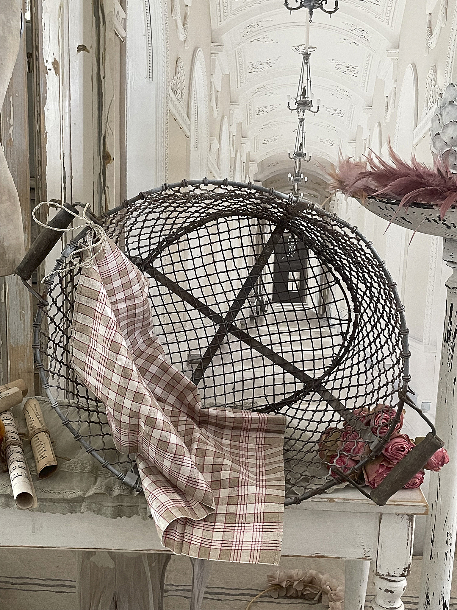 Dekorativer Drahtkorb mit Textil und Accessoires Drahtkorb mit kariertem Stoff und Rosen auf einem vintage Tisch