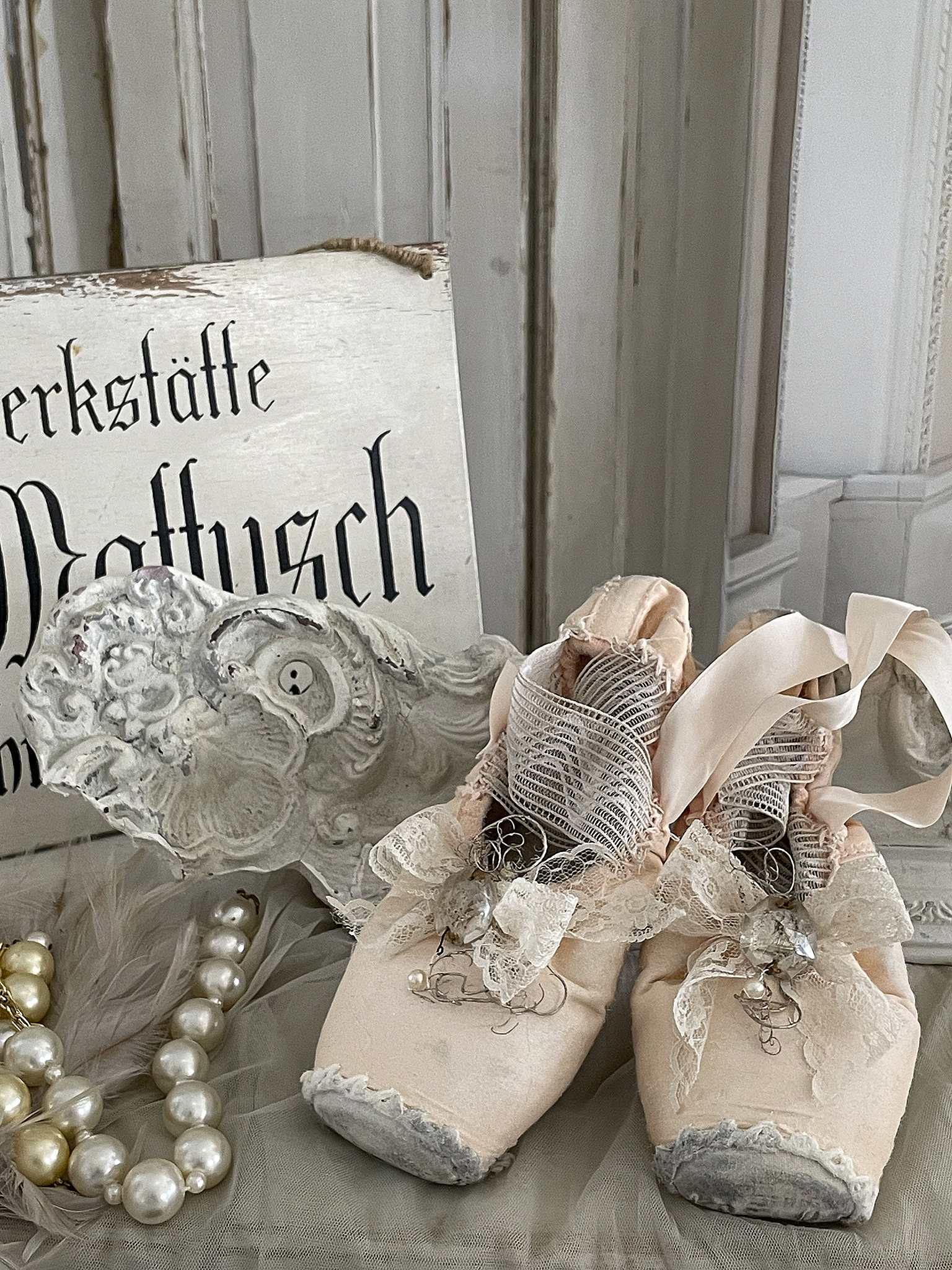 Antike rosa Ballettschuhe mit dekorativen Details neben einer Perlenschnur und einer nostalgischen Deko