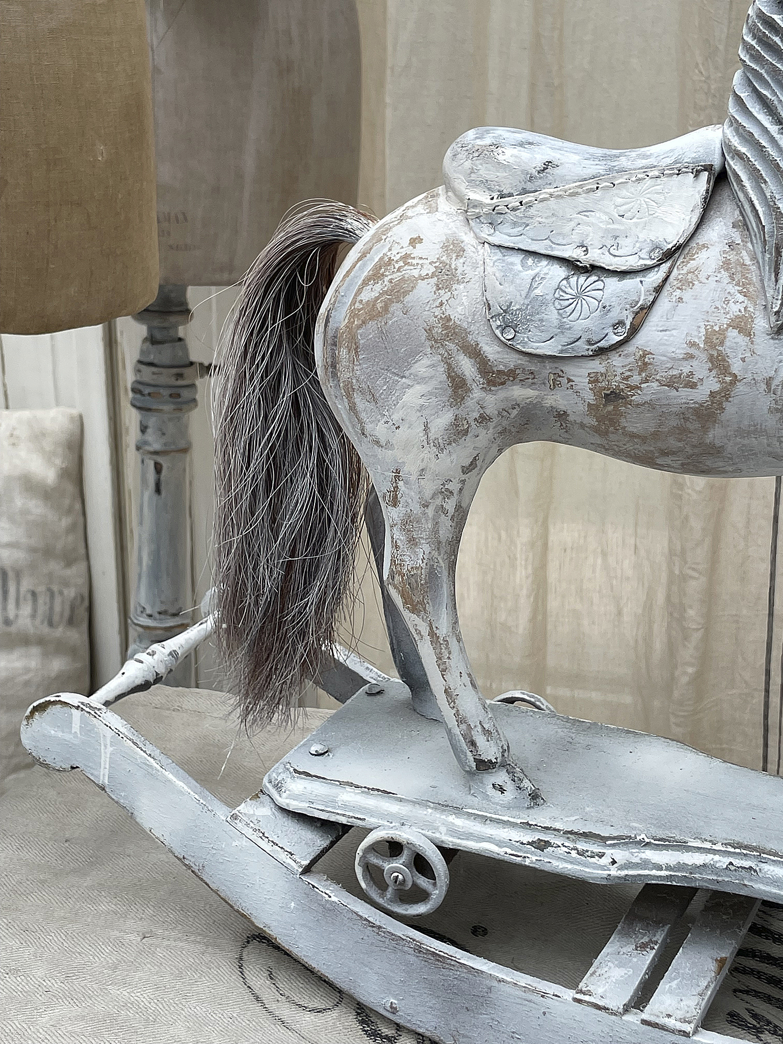 Detailaufnahme eines antiken Holzschaukeltieres in grau mit einem Sattel und elegantem Schweif