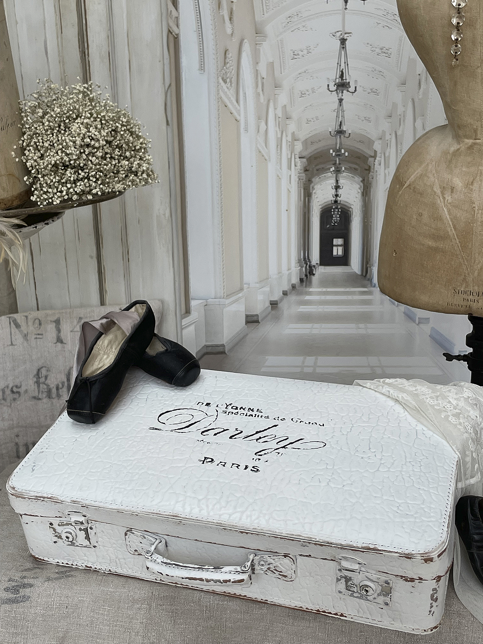 Elegante weiße Reisekoffer mit Ballettschuhen und Deko Weißer Koffer mit Aufschrift von Paris, neben Ballettschuhen und einer Schneiderpuppe