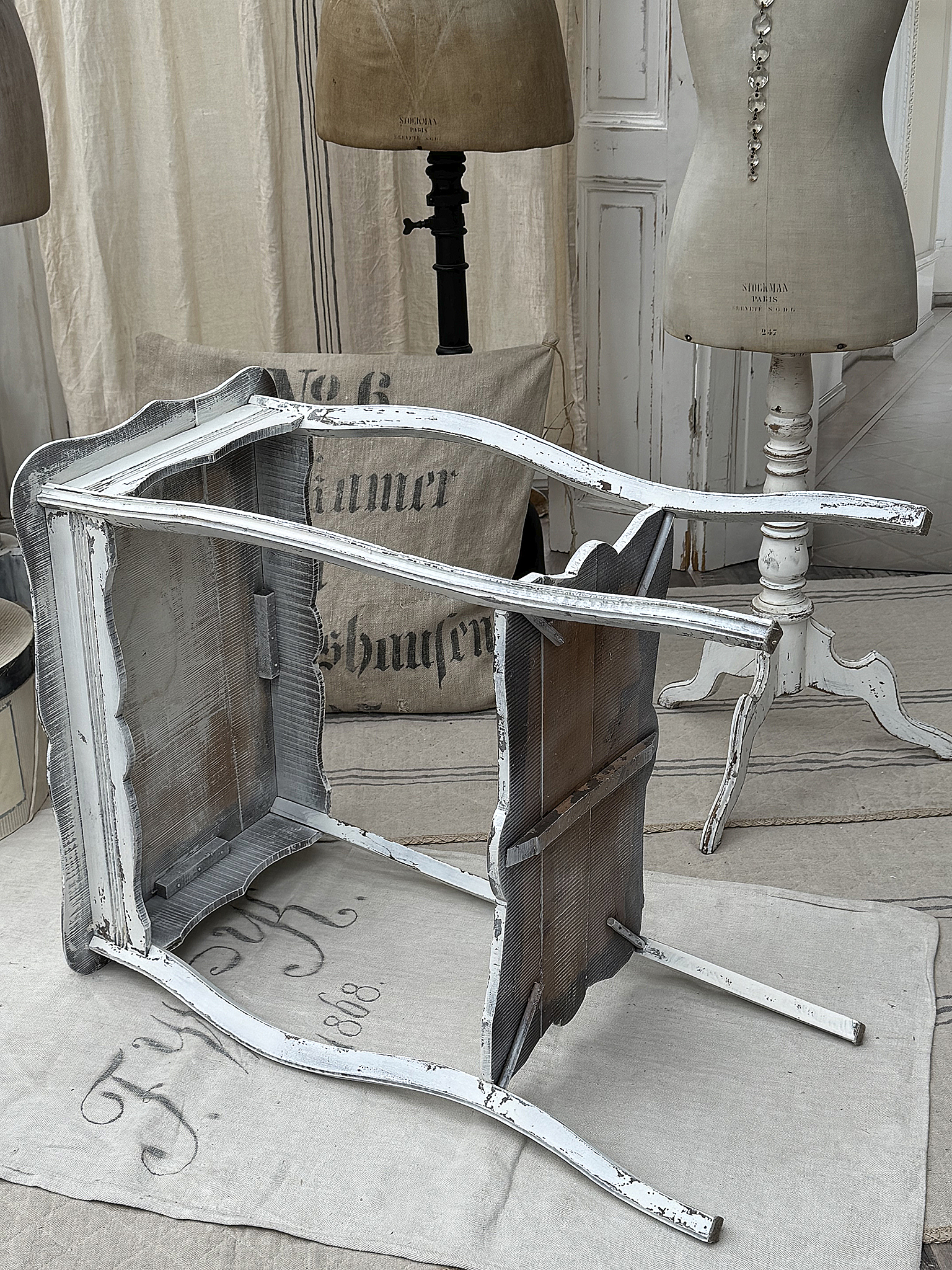 Antiker weißer Tisch im Vintage-Stil Glatter, antiker Tisch in weißem Finish mit Vintage-Charme, umgeben von Schneiderpuppen.