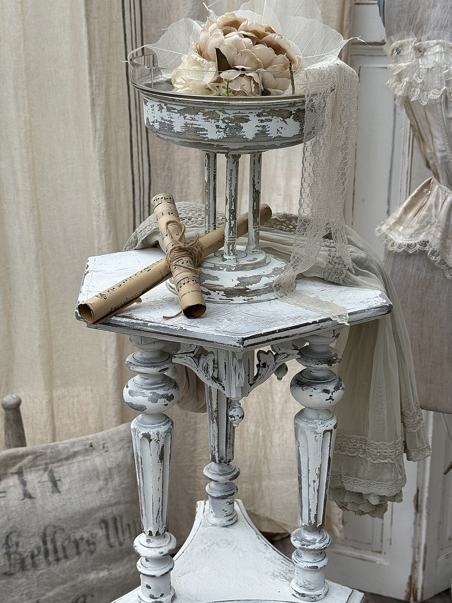 Dekorativer Beistelltisch mit Blumenarrangement und Dekorationsrollen Beistelltisch im Shabby-Chic-Stil mit einer Glasschale voller Blumen und dekorativen Rollen
