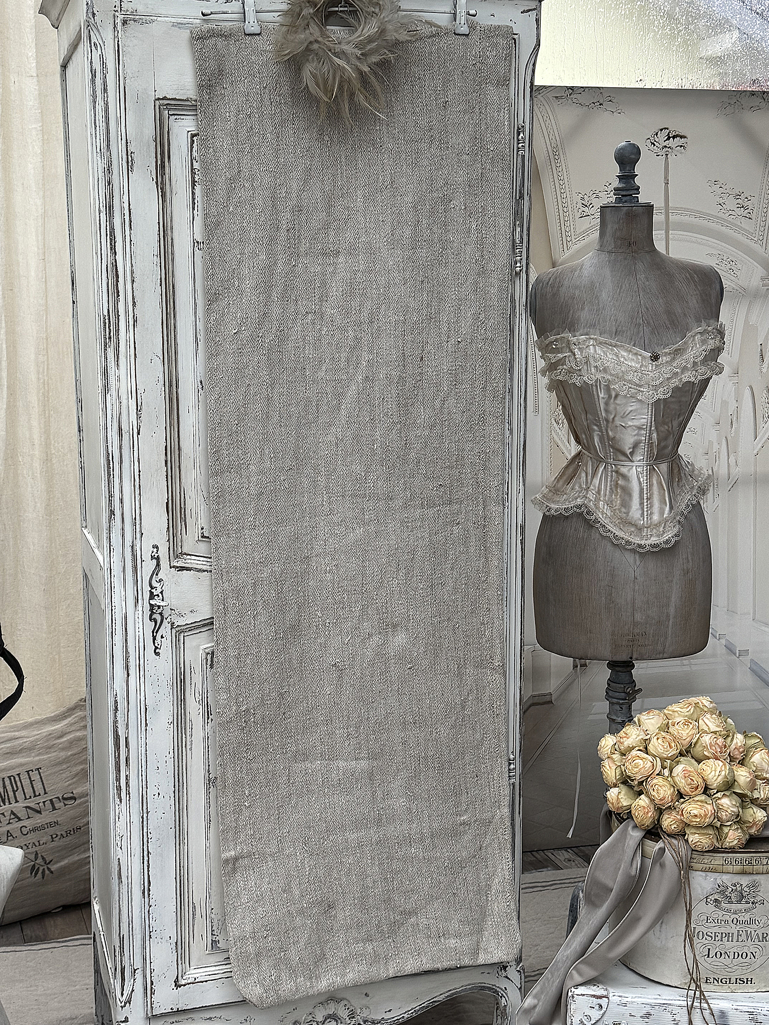 Dekorative Leinenwand vor einem antiken Schrank, daneben eine Corsage und ein Blumenstrauß