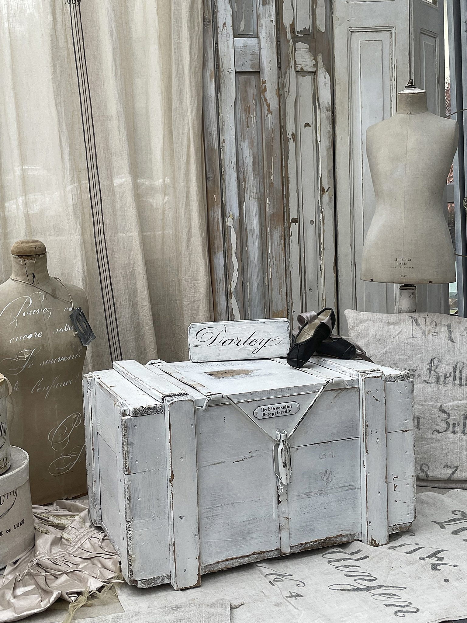 Antike Holzkiste mit vintage Charme als stilvolle Dekoration Holzkiste im Shabby-Chic-Stil, dekoriert mit weißen Stoffen und einer Schneiderpuppe
