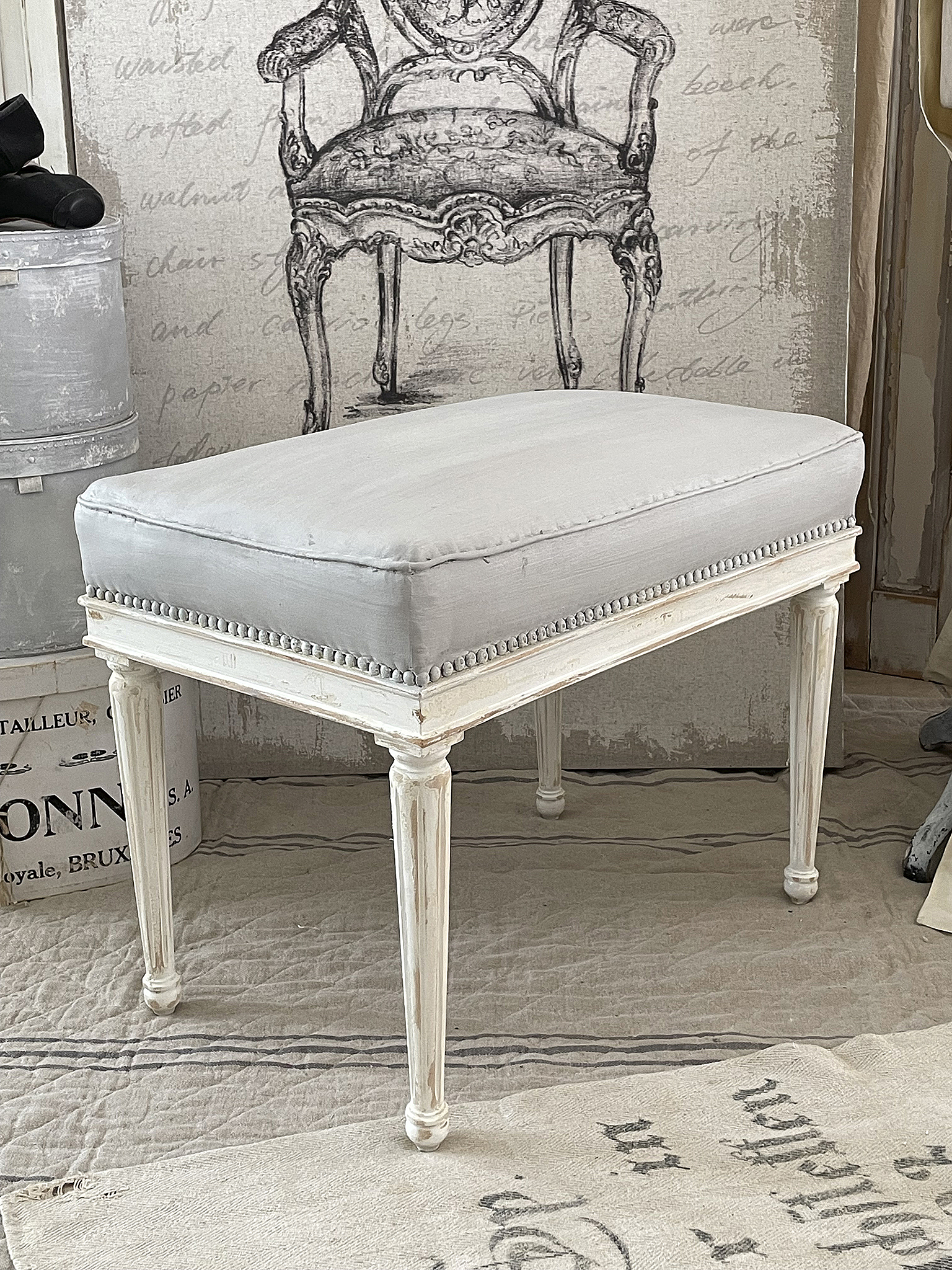 Eleganter Hocker mit gepolstertem Sitz in Grau Schöner Hocker mit weißen Beinen und grauem gepolstertem Sitz