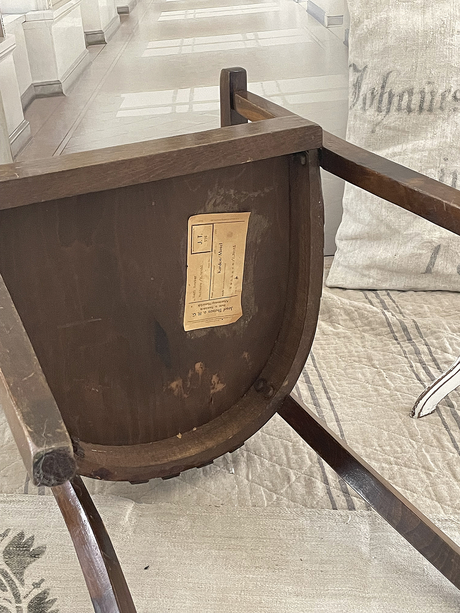 Antiker Holzstuhl mit Etikett auf der Unterseite Detailaufnahme eines Holzstuhls mit Etikett, der auf einer Stoffunterlage steht.