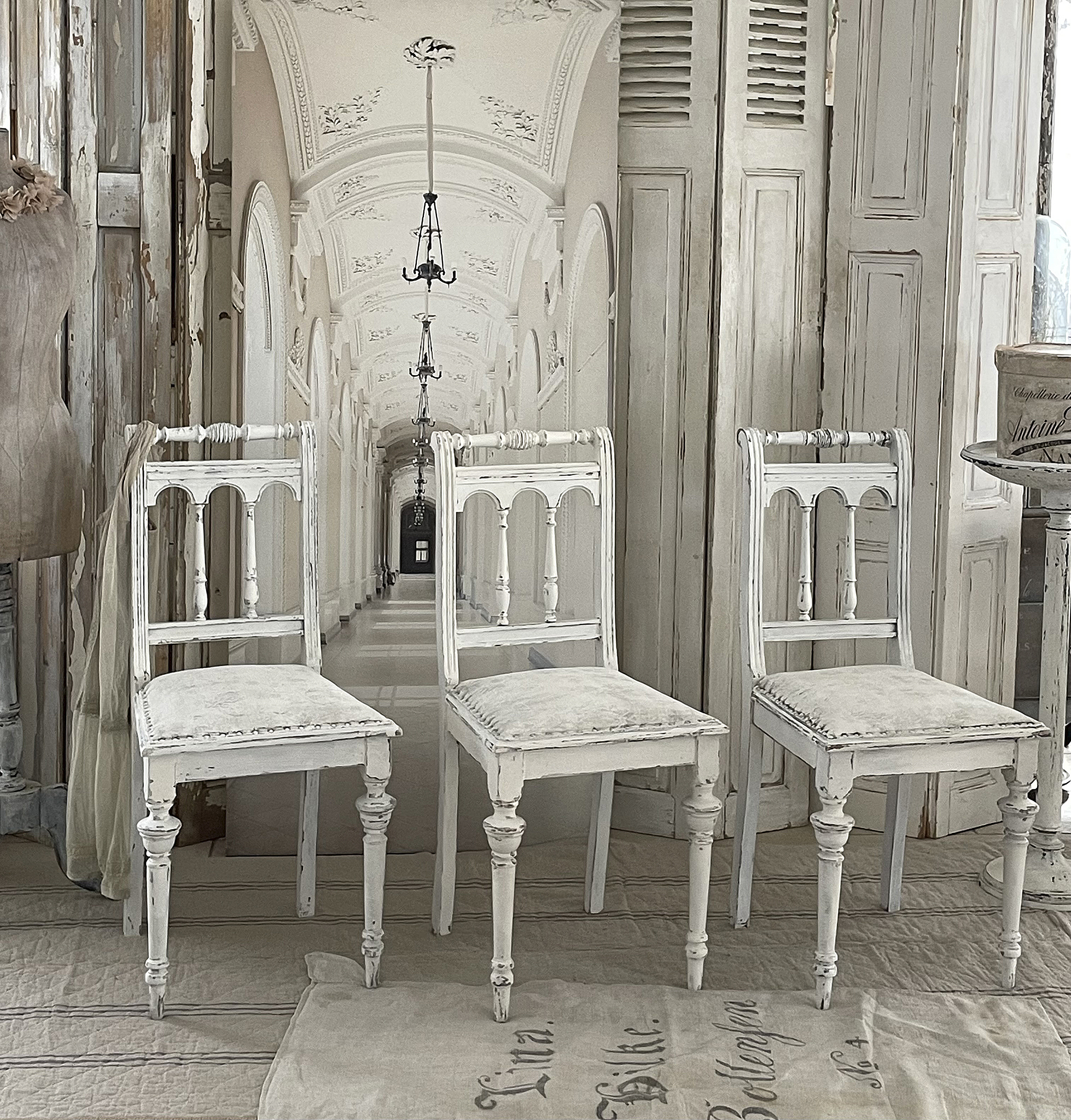 Drei elegante weiße Stühle in einem stilvollen Innenraum Drei weiße Stühle im Vintage-Stil vor einem schönen, hellen Flur