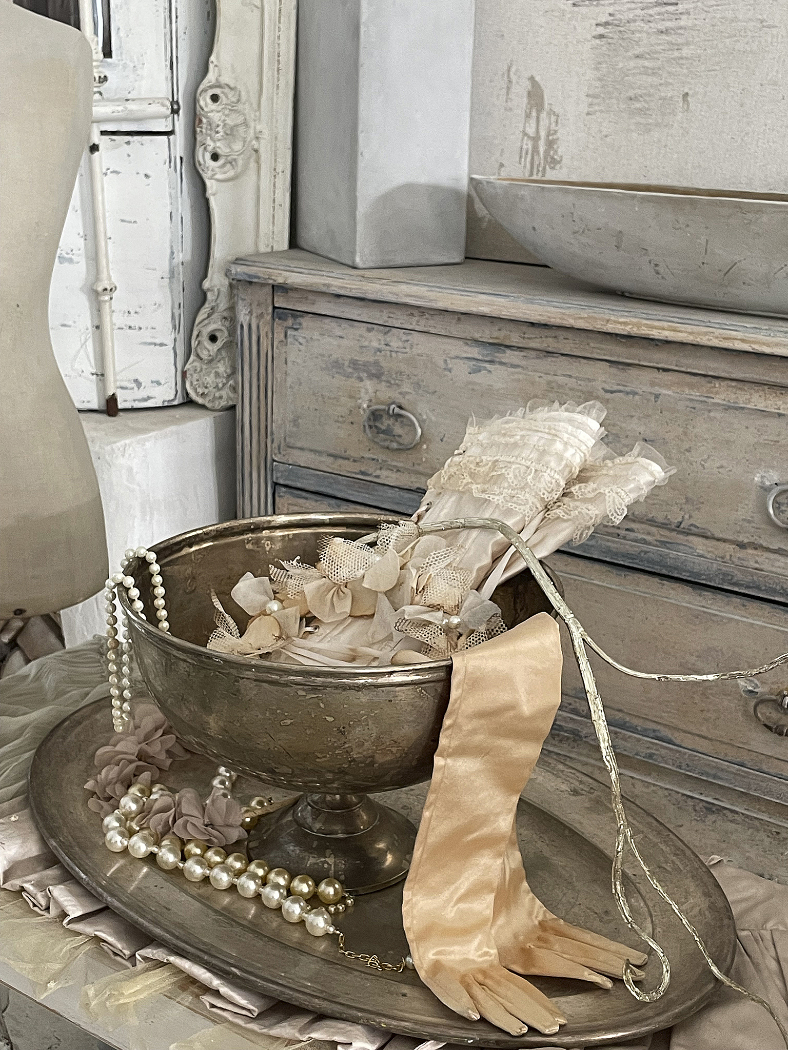 Elegante Accessoires in einer nostalgischen Inneneinrichtung Schöne Accessoires in einer silbernen Schale, darunter Perlen, Bänder und Handschuhe auf einem Vintage-Tisch.