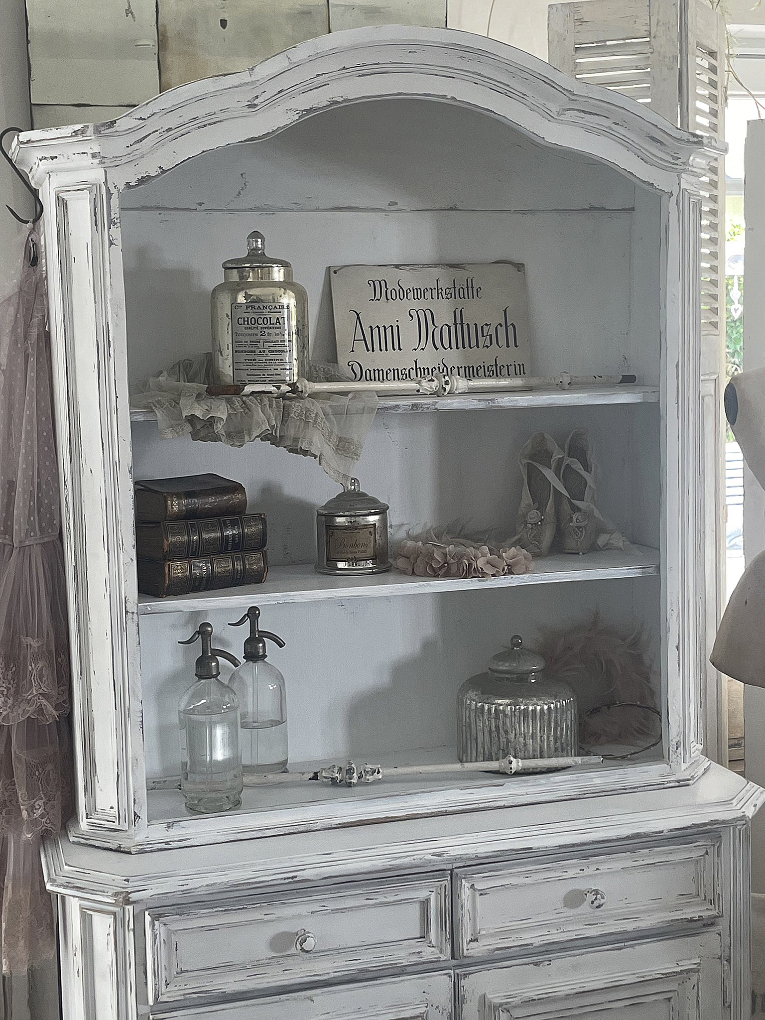 Vintage Vitrine mit historischen Utensilien und eleganten Details Detailansicht einer antiken Vitrine mit Flaschen, Büchern und einem Schild der Schneiderin Anni Matthusch.