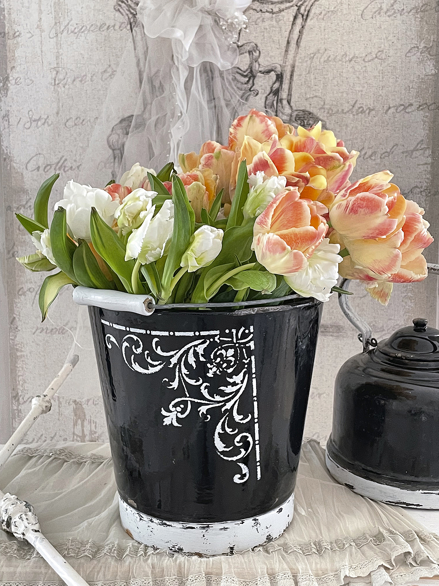 Schwarz-weiß dekorierter Eimer voller leuchtender Tulpen und anderen Blumen auf einem romantischen Hintergrund