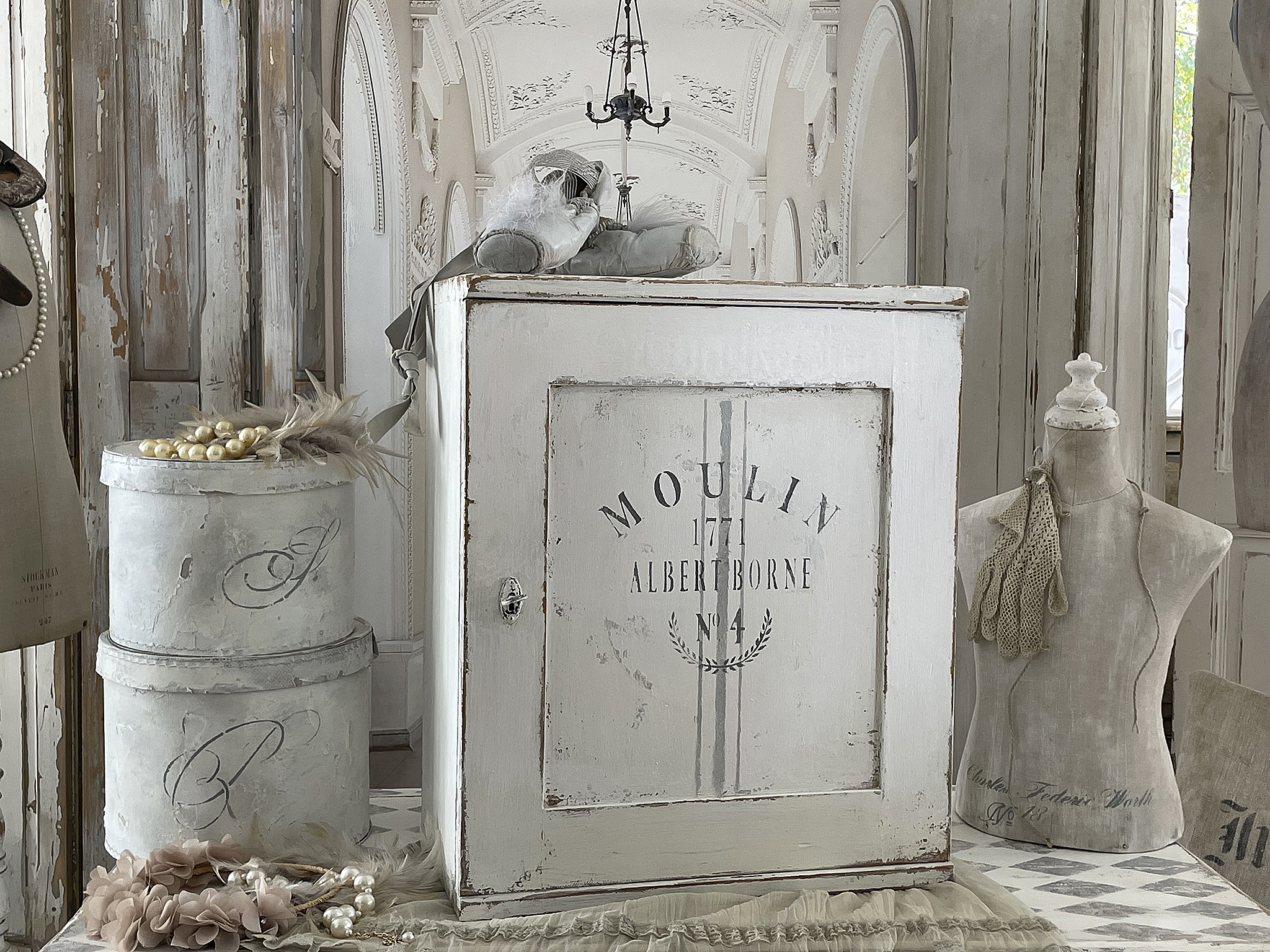 Charmanter vintage Schrank im französischen Landhausstil Ein eleganter weißer Schrank mit dem Schriftzug 'Moulin' im französischen Landhausstil, umgeben von Accessoires.