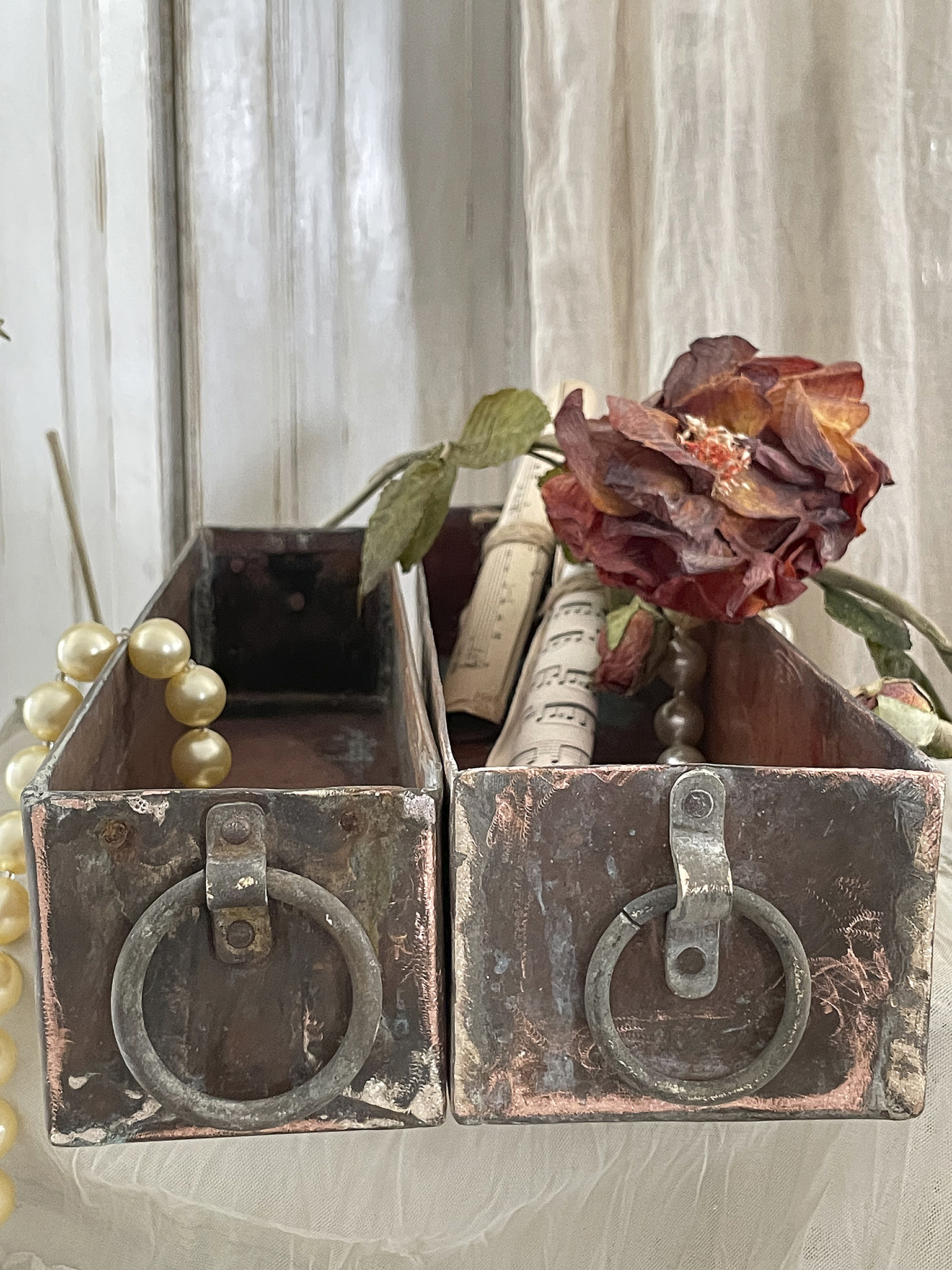 Dekorative Metallkästchen mit Vintage-Rose und Noten Zwei rustikale Metallkästchen mit einer verwelkten Rose und Notenrollen, umgeben von Perlen.