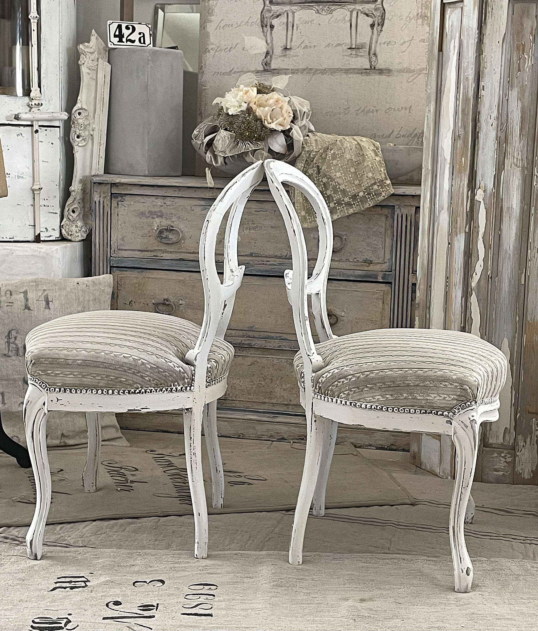 Zwei stilvolle weiße Stühle im Vintage-Look mit gestreiften Polstern Zwei elegante weiße Stühle mit einem antiken Design und gestreiften Polstern, die in einem wohnlichen Ambiente präsentiert werden.