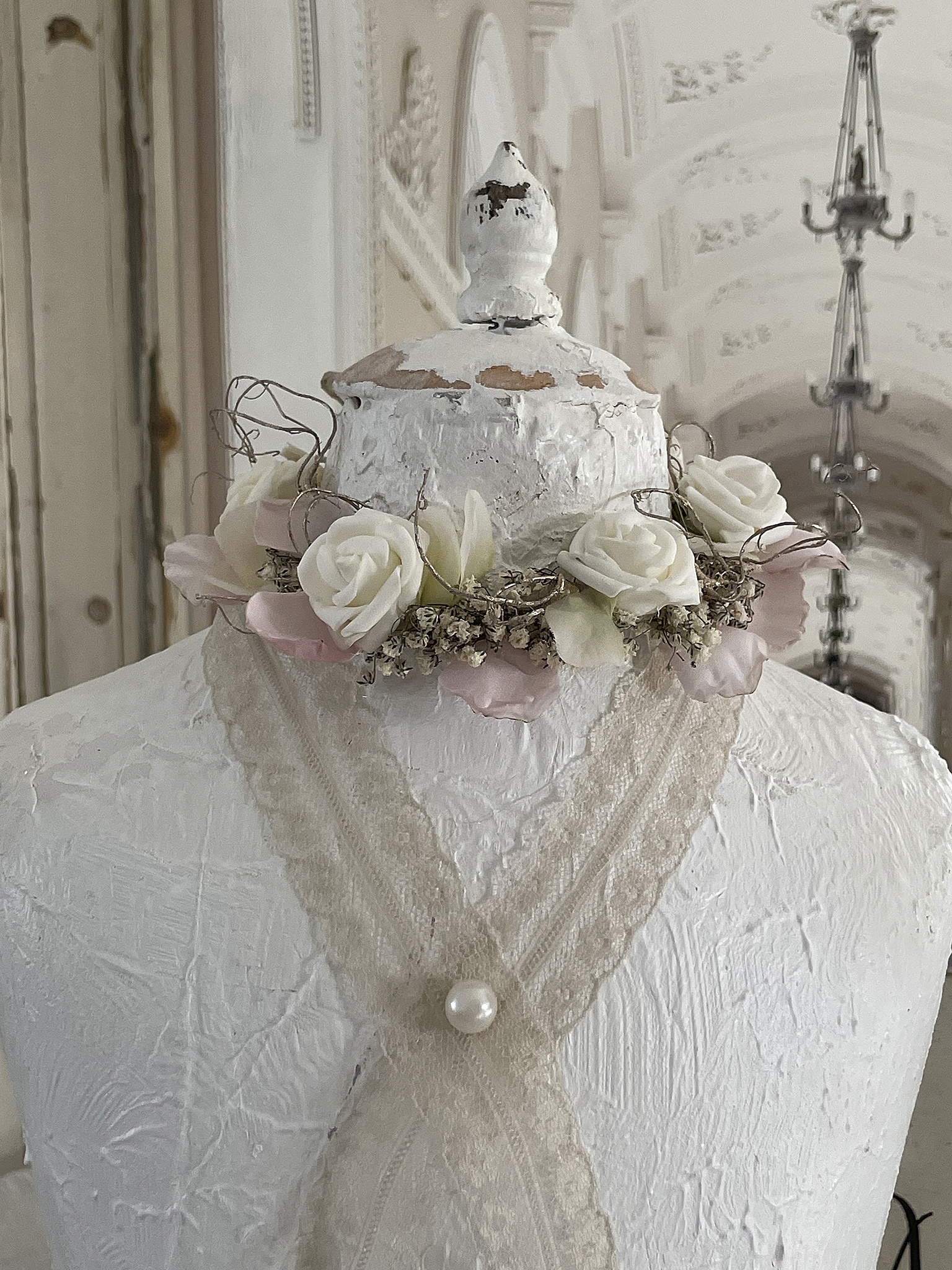 Vintage Mannequin mit Blumenkranz und Spitzendekoration Weißer Vintage-Mantel mit floralem Kranz und Spitze im Hintergrund einer eleganten Innenarchitektur