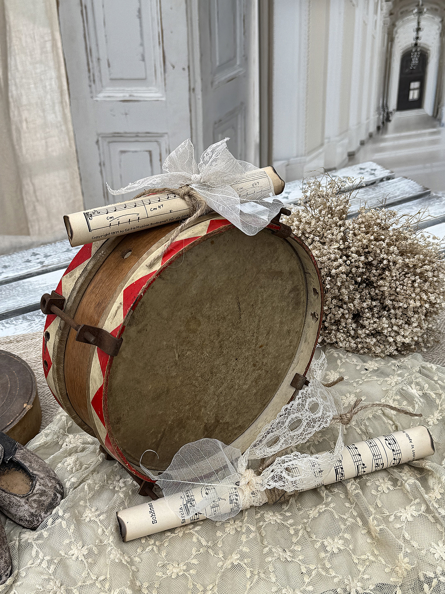 Dekorative Trommel mit Notenpapier und getrockneten Blüten auf einem eleganten Stoff