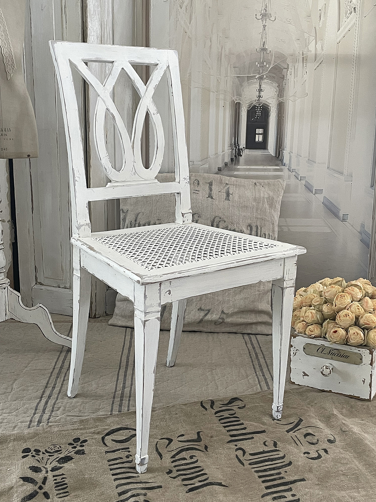 Weißer Vintage-Stuhl mit Rattan-Sitzfläche Rustikaler weißer Stuhl mit elegantem Design und Rattanoberfläche auf einem dekorativen Stoffhintergrund.