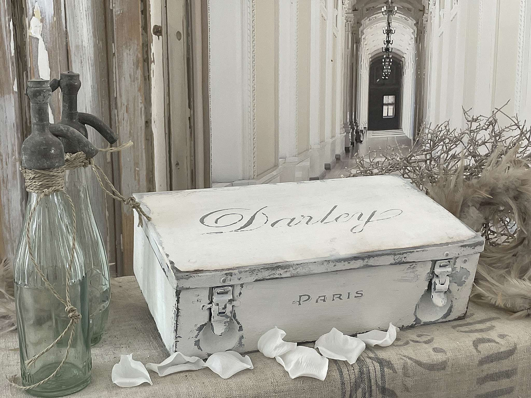 Vintage Aufbewahrungskiste Darley aus Paris mit nostalgischem Flair Nostalgische Aufbewahrungskiste Darley aus Paris, umgeben von dekorativen Flaschen und Blütenblättern
