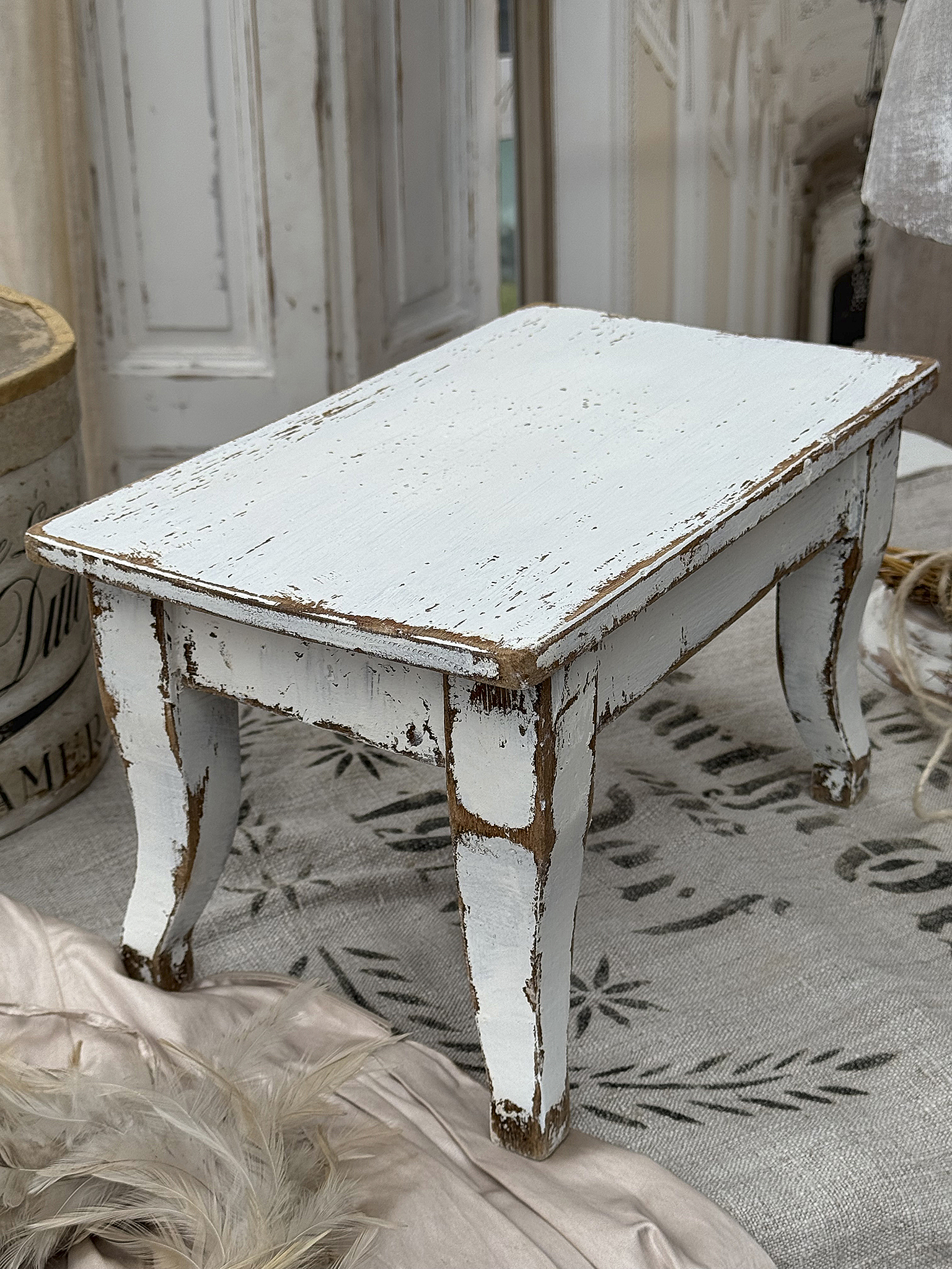 Antiker Hocker im Landhausstil in sanftem Weiß Kleiner vintage Hocker mit abgenutzter weißer Farbe und geschwungenen Beinen