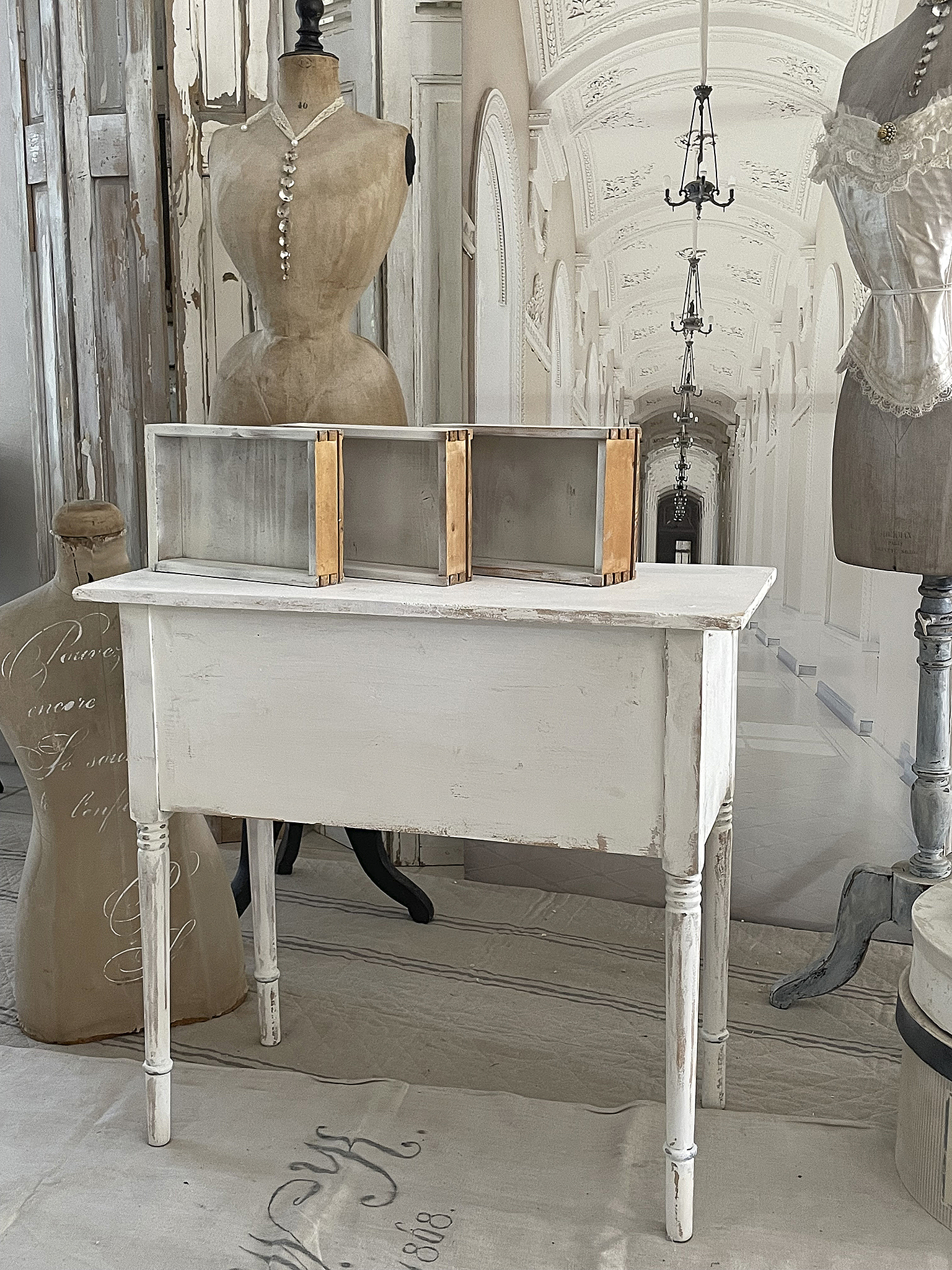 Weißes Konsolentisch im Vintage-Stil mit Holzdetails Vintage Konsolentisch aus Holz, dekoriert mit einer Schneiderpuppe und einem rustikalen Hintergrund