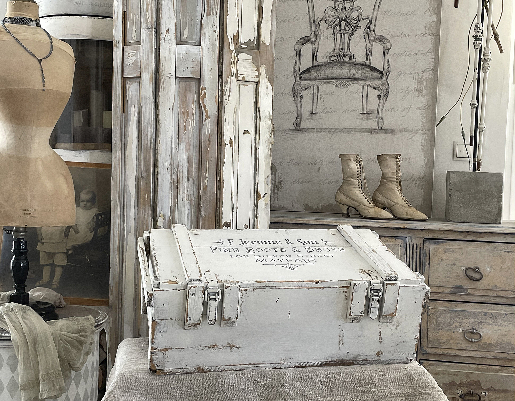 Charmante antike Holztruhe mit Vintage-Stil und alten Stiefeln Antike Holztruhe mit dem Schriftzug 'F. Jerome & Son' und nostalgischen Stiefeln im Hintergrund