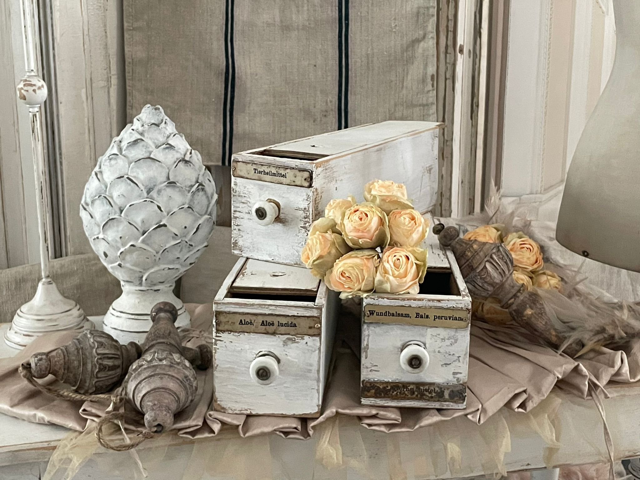 Detailaufnahme von dekorativen Vintage-Objekten, darunter Schubladenkästchen, künstliche Rosen und eine schöne Zapfenfigur.