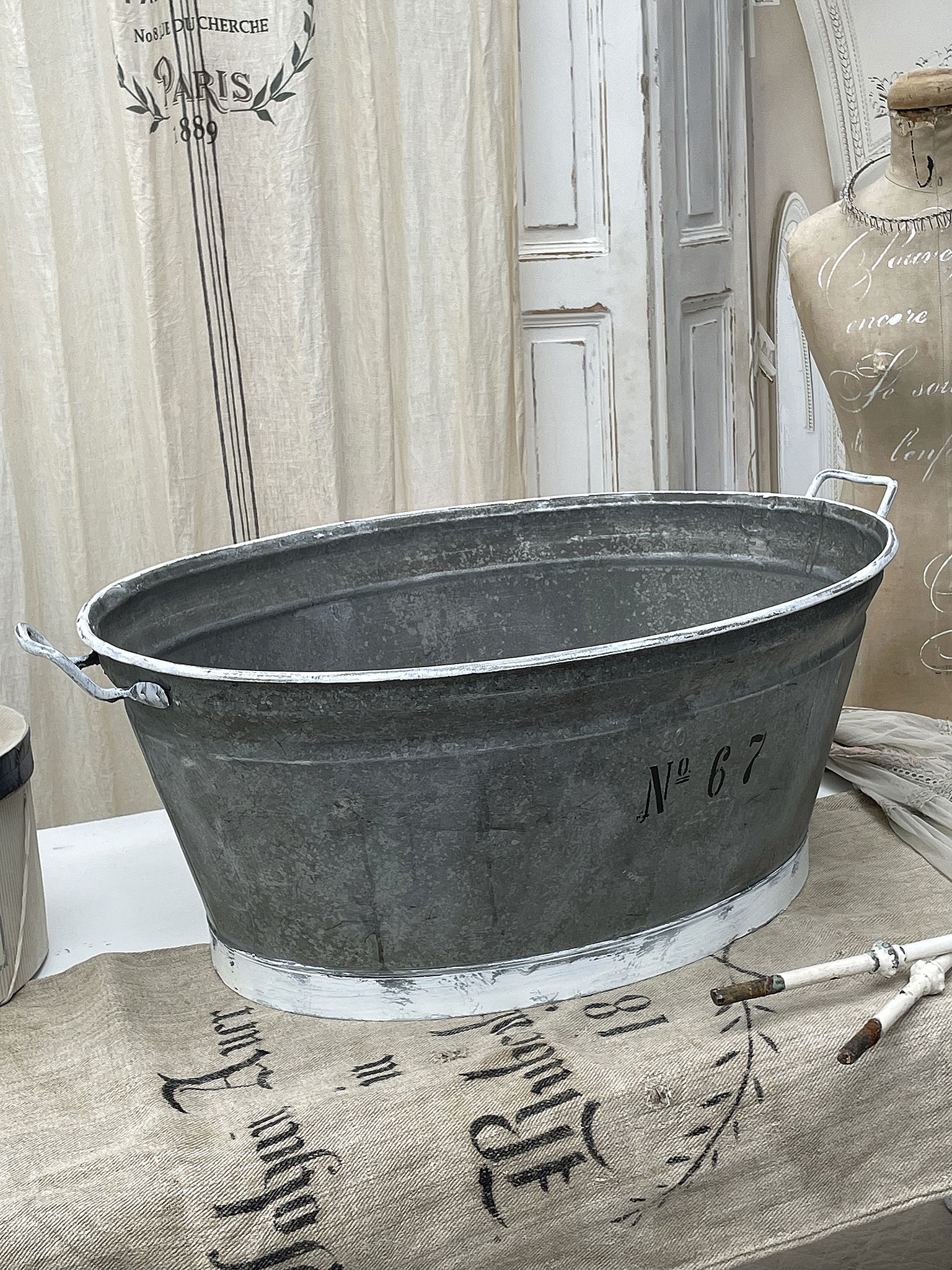 Runde Zinkwanne mit Griffelementen und Nummer 67 Zinkwanne in rundem Design mit der Aufschrift Nummer 67, auf einem vintage-inspirierten Tisch dekoriert.