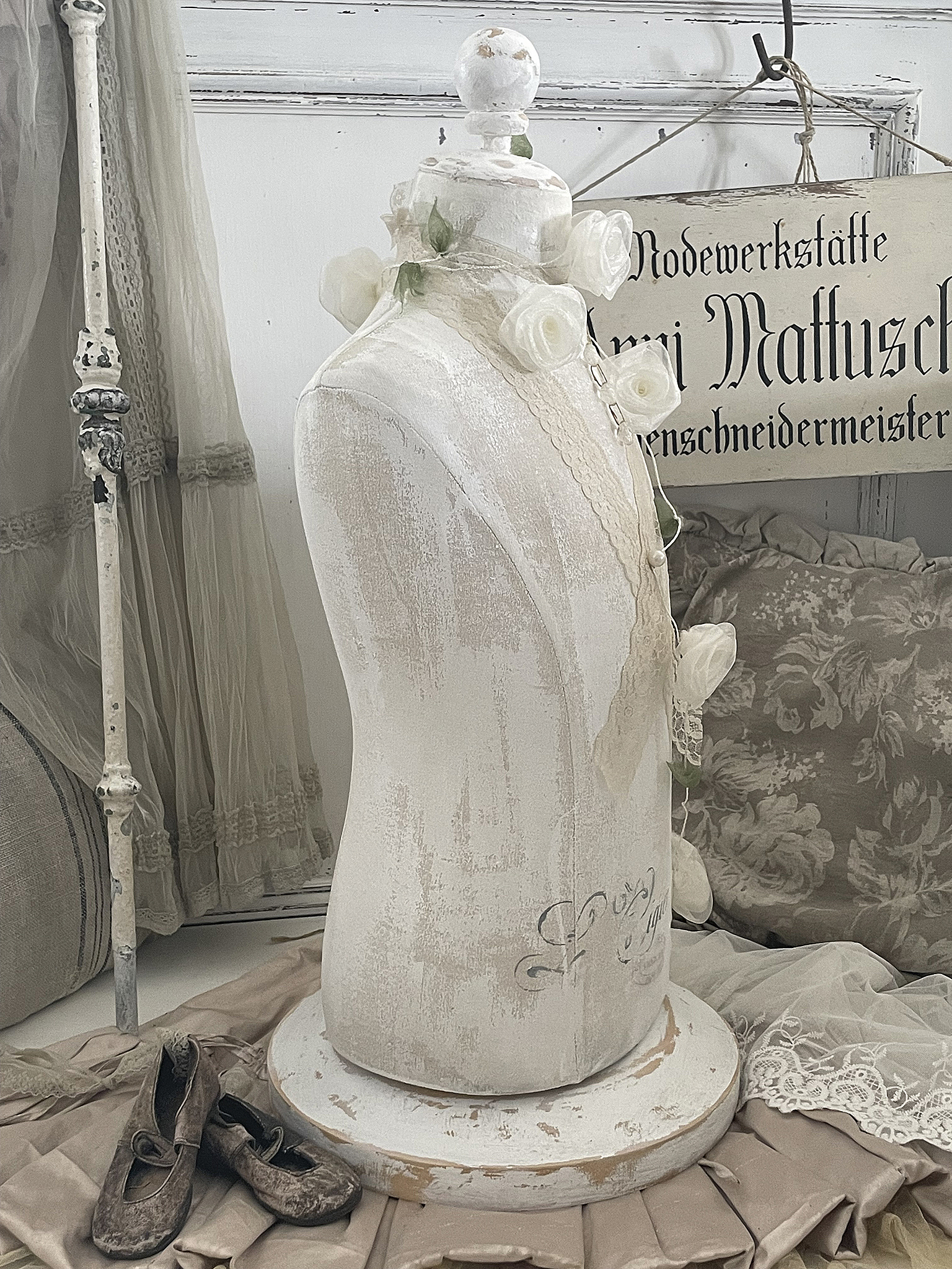 Elegantes Schneiderpuppe mit Blumen und Vintage-Details Schneiderpuppe in Weiß mit Rosen und alten Schuhen auf einem Stoffhintergrund